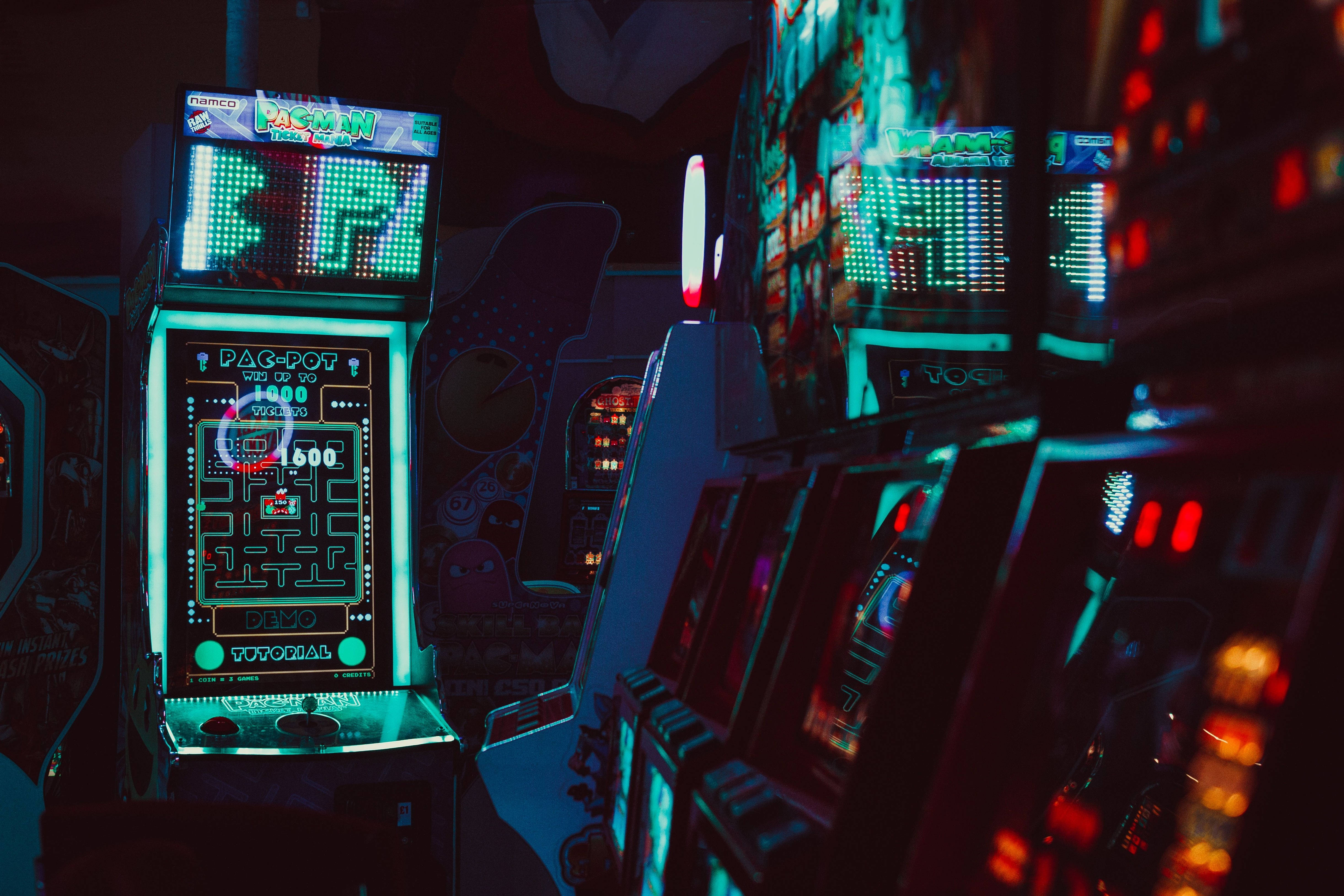 遊戲 桌布 壁紙 — 充滿活力的霓虹燈街機在昏暗的遊戲廳中發光，發光的 Pac-Man 機櫃成為焦點。