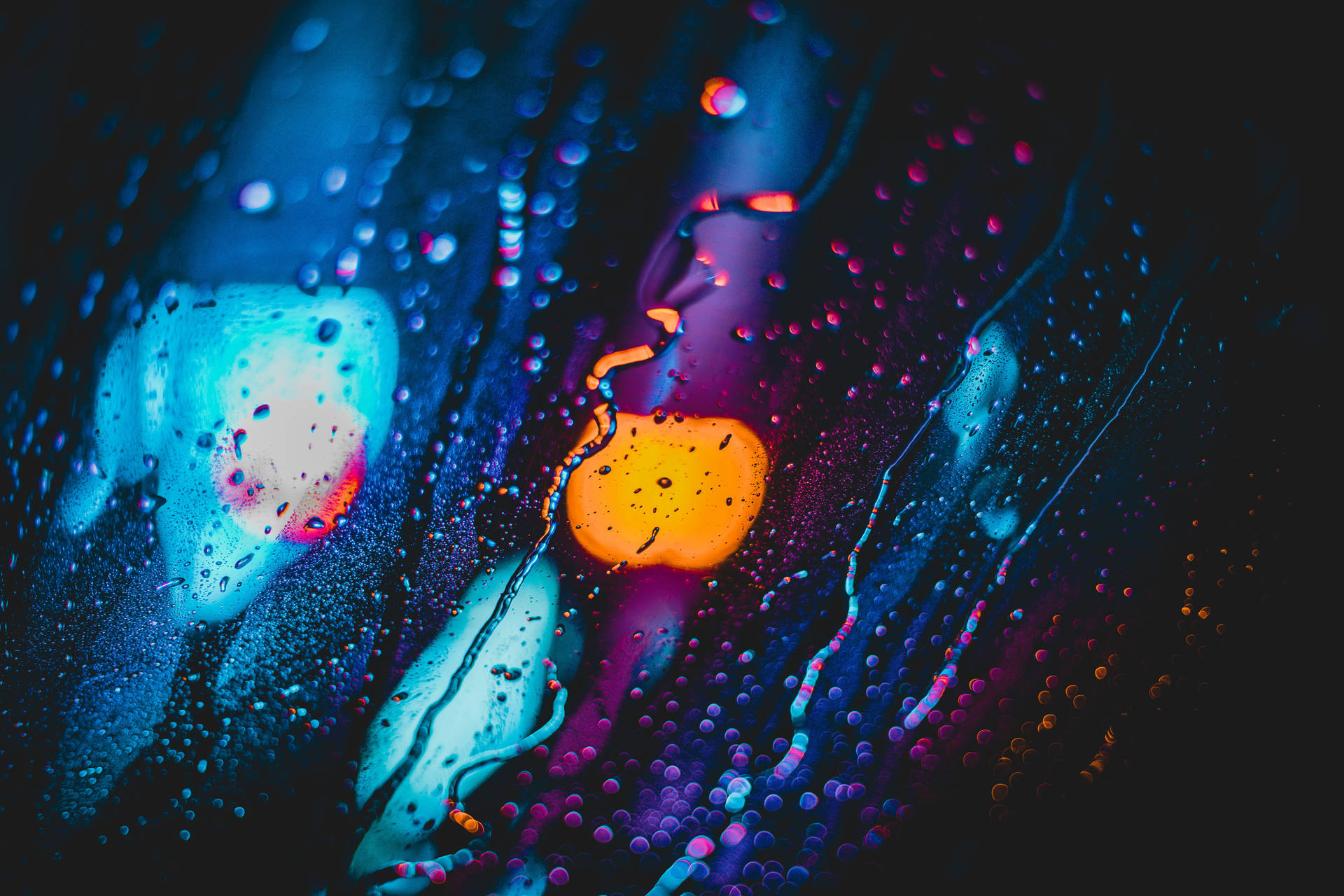 夜晚霓虹燈在玻璃上反射出鮮豔色彩的雨滴。