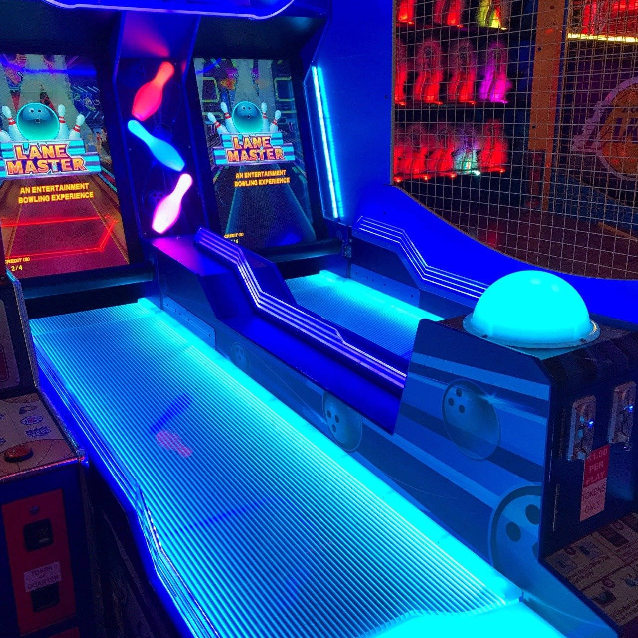 arcade 桌布 壁紙 — 充滿活力的霓虹藍色街機保齡球館，配有發光球道和復古遊戲螢幕，位於熱鬧的娛樂中心。