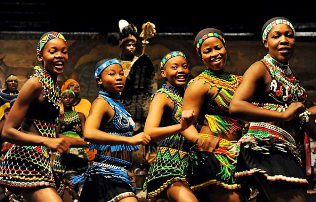 African Culture 桌布 壁紙 — 充滿活力的非洲舞者身穿色彩繽紛的珠飾，在舞台燈光下以富有表現力的笑容和動感姿態歡樂地表演。