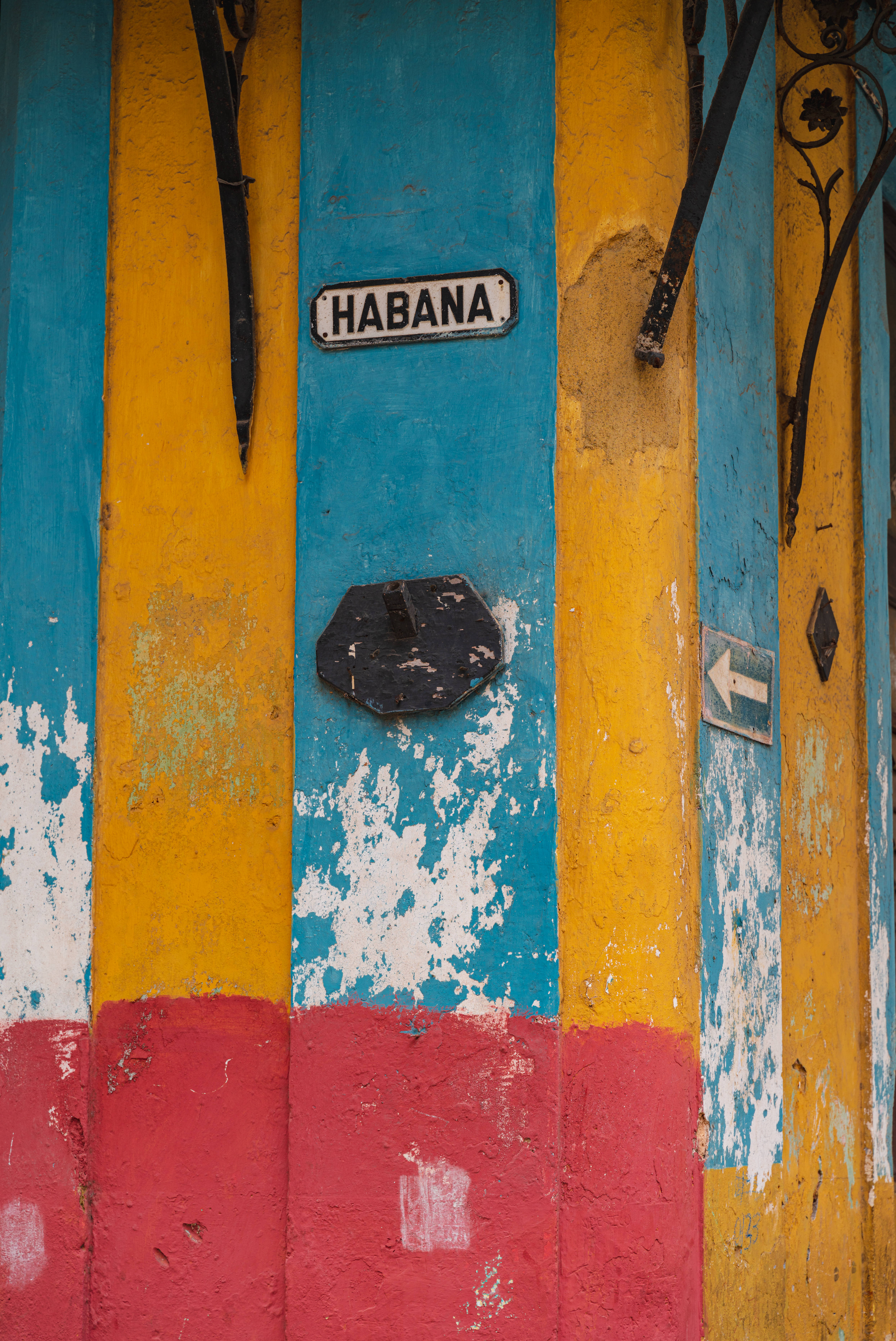 Cuba 桌布 壁紙 — 充滿活力的風化木門，帶有鮮明的黃、藍、紅條紋，設有「HABANA」標誌和華麗的黑色金屬製品。