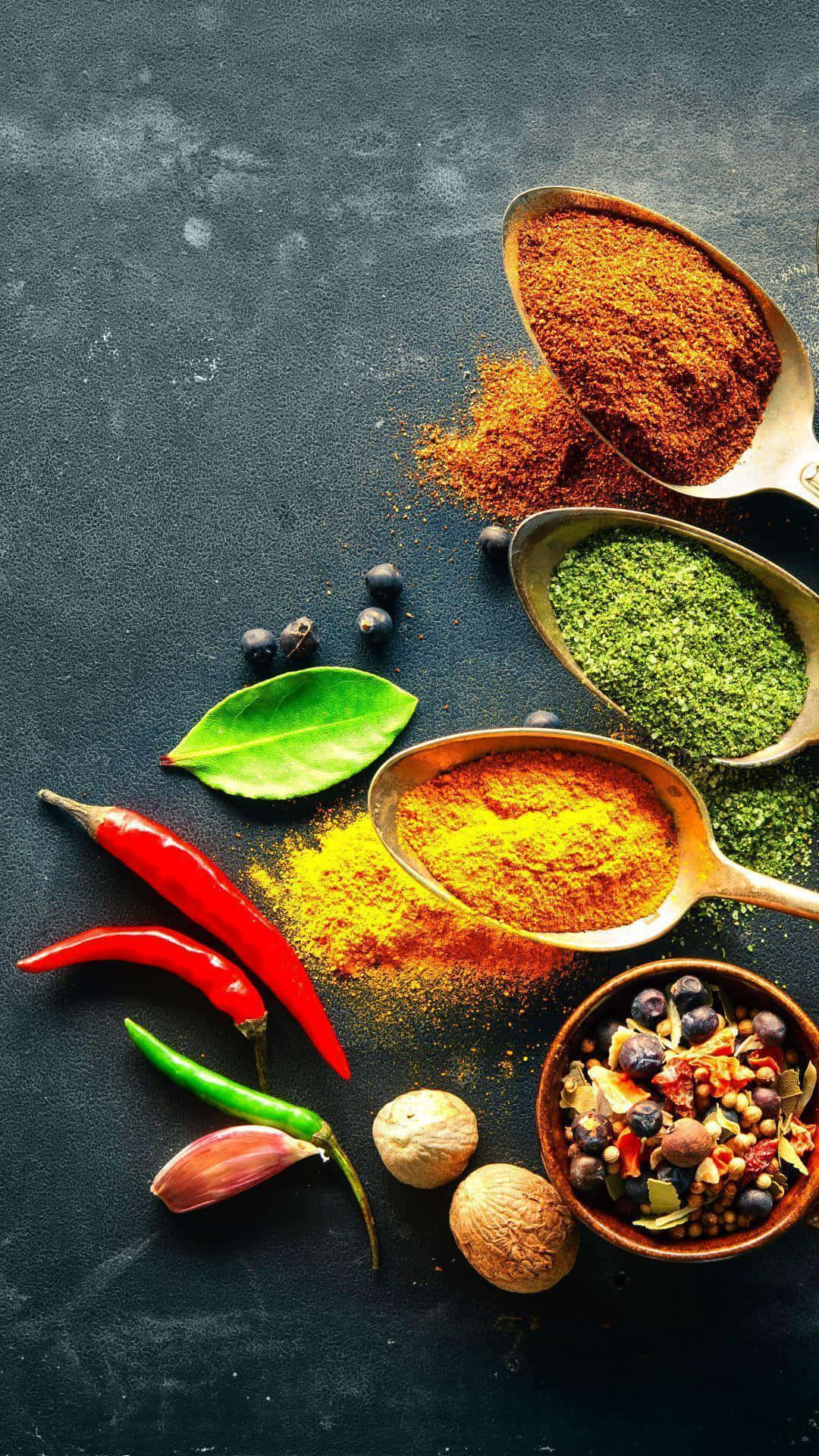 Spices 桌布 壁紙 — 充滿活力的香料和香草從湯匙和碗中溢出，落在深色紋理表面上。