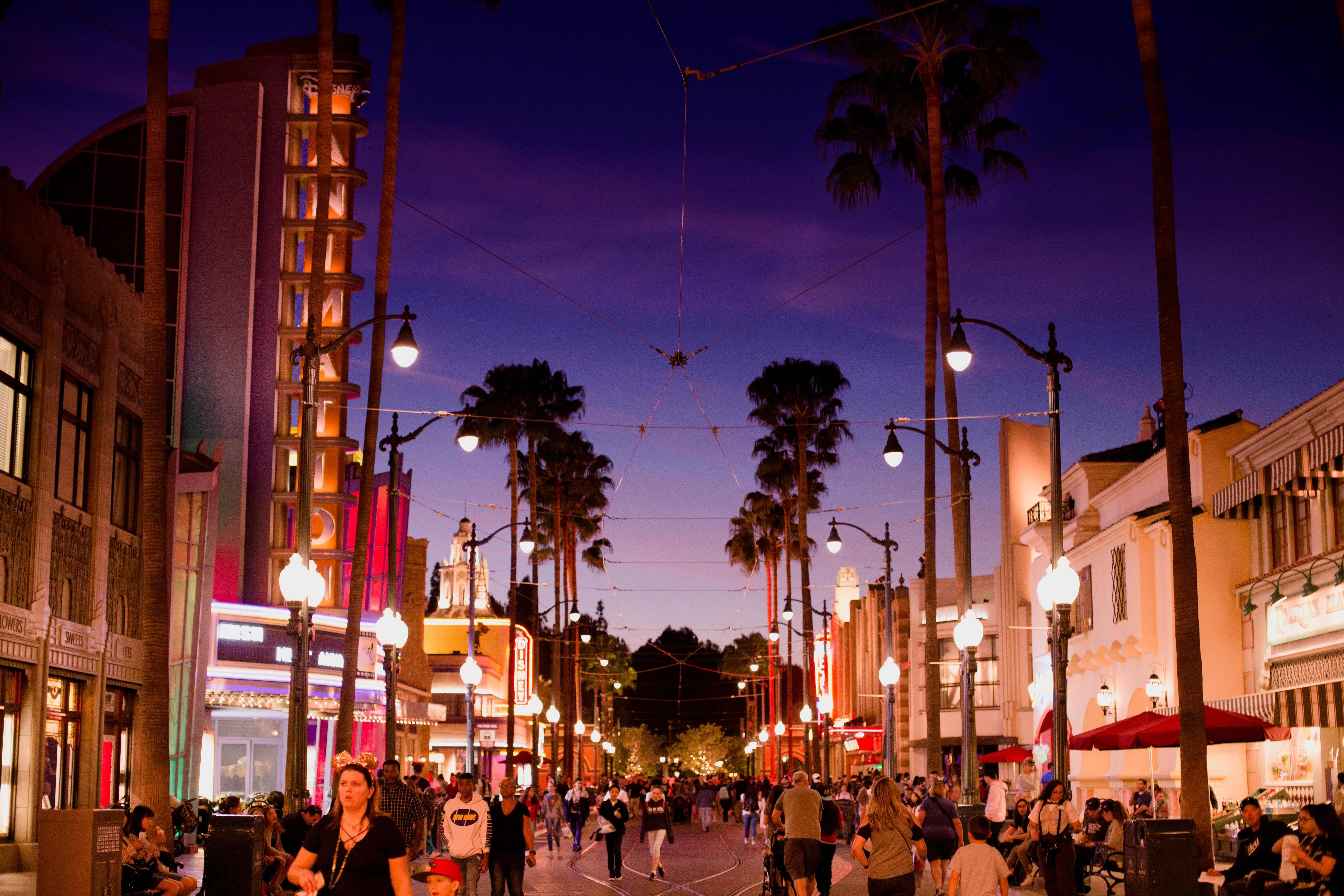 hollywood street 桌布 壁紙 — 充滿活力的黃昏街景，棕櫚樹、閃爍的路燈和人群享受熱鬧的城市長廊。