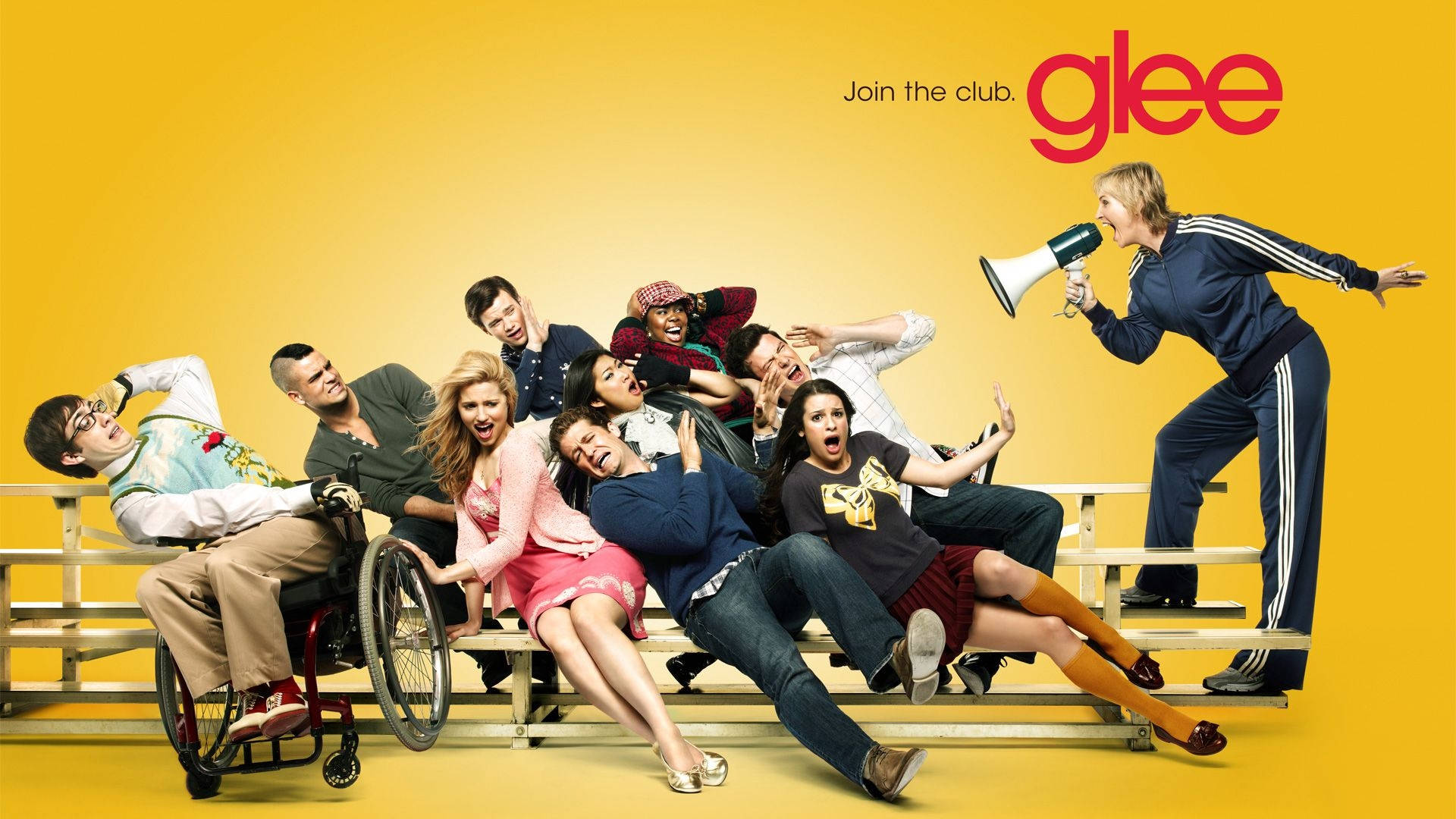 tv 桌布 壁紙 — 充滿活力的黃色背景上，Glee 演員們在觀眾席上充滿活力地擺姿勢，教練透過擴音器大喊。