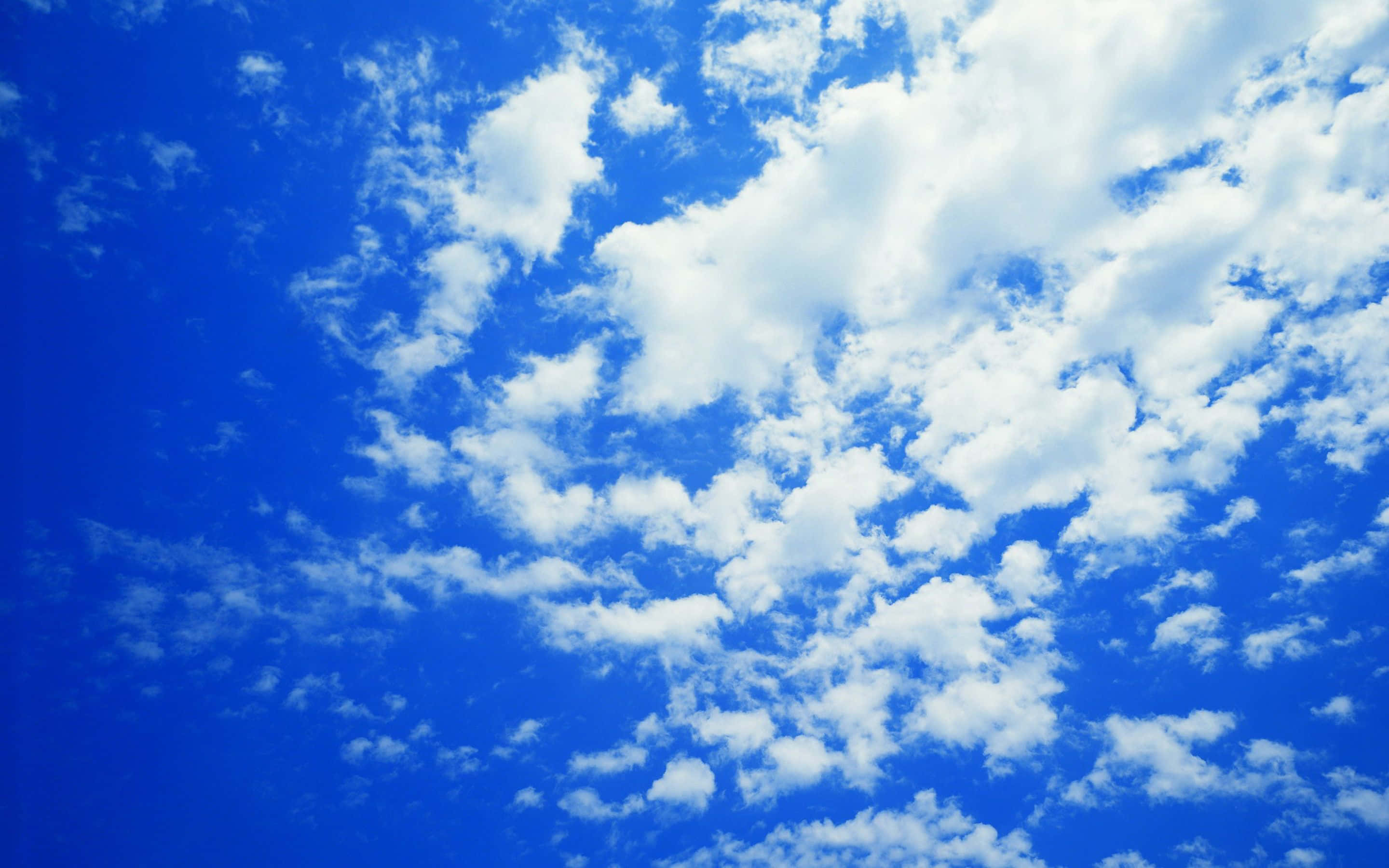 Blue Skies 桌布 壁紙 — 充滿蓬鬆白雲的鮮豔藍天，在晴朗的白天天空中飄移。