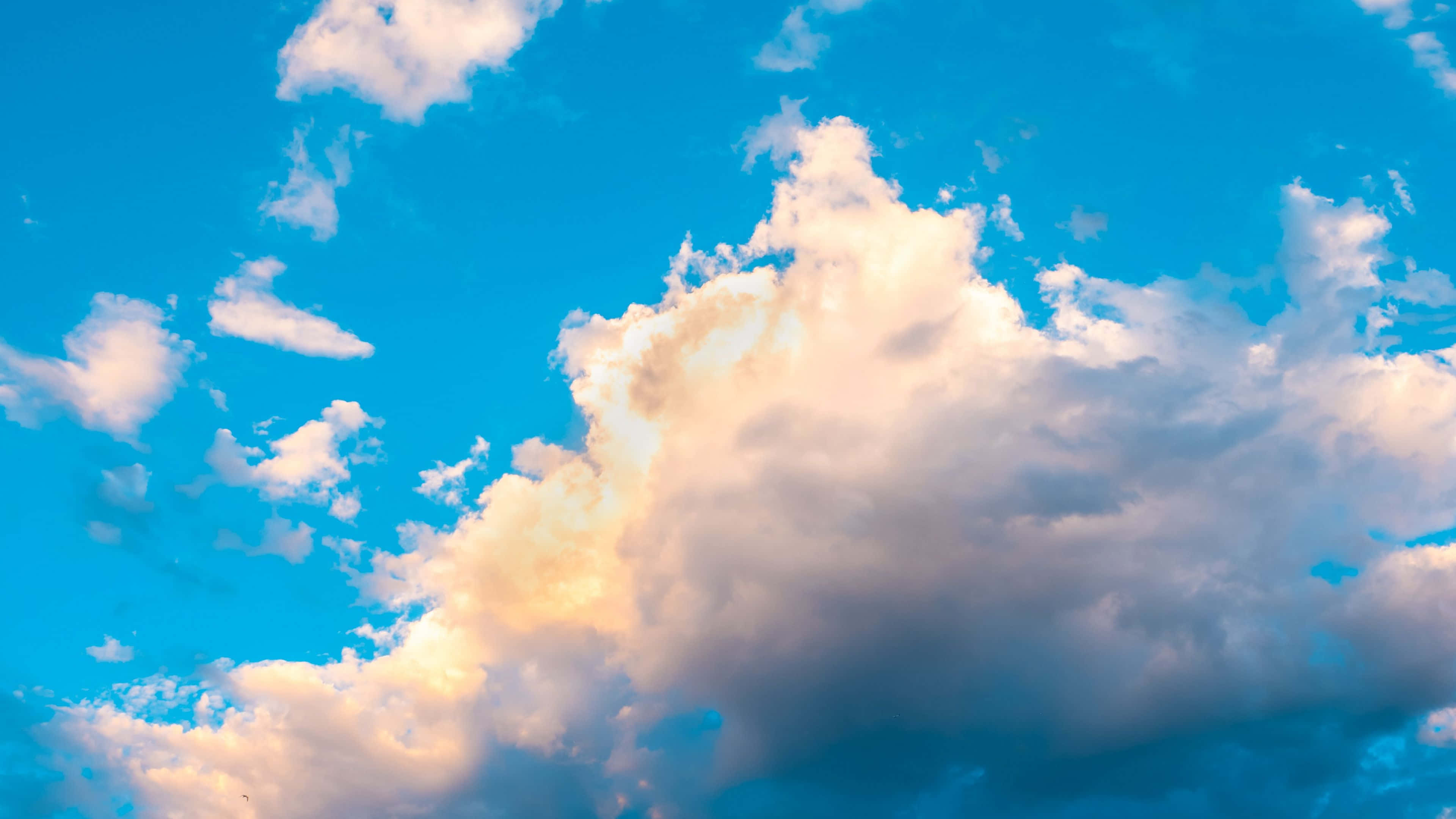Clouds Aesthetics 桌布 壁紙 — 充滿蓬鬆白雲的鮮豔藍天，在金色陽光下閃耀。