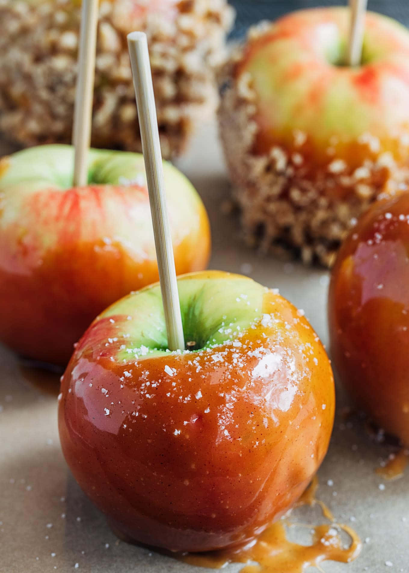 Caramel Apples 桌布 壁紙 — 光亮焦糖包裹的蘋果，撒上海鹽，放在鋪有烘焙紙的托盤上，附有木棒。