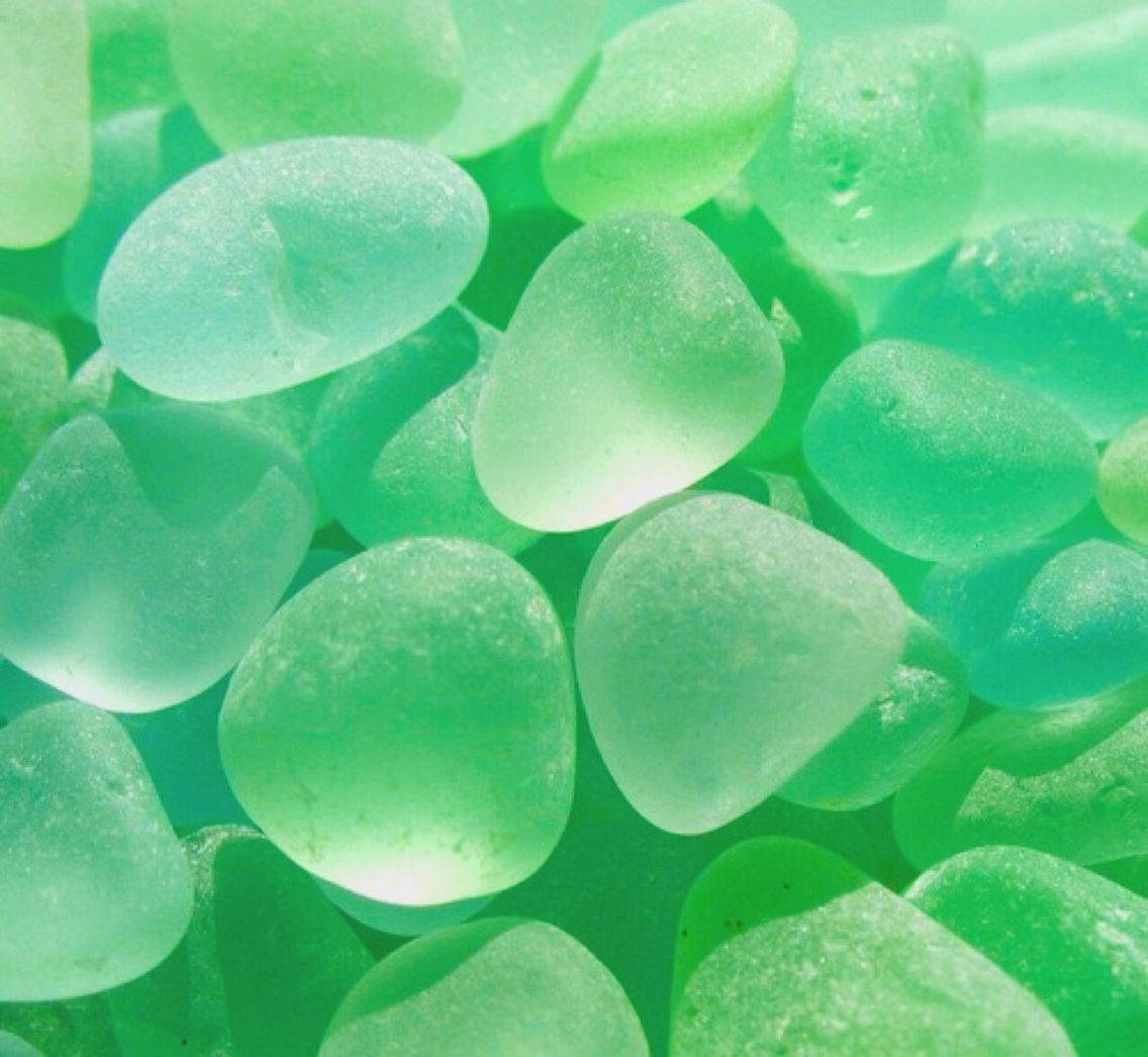 美學 桌布 壁紙 — 光滑半透明綠色海玻璃卵石在明亮光線下柔和發光的特寫。