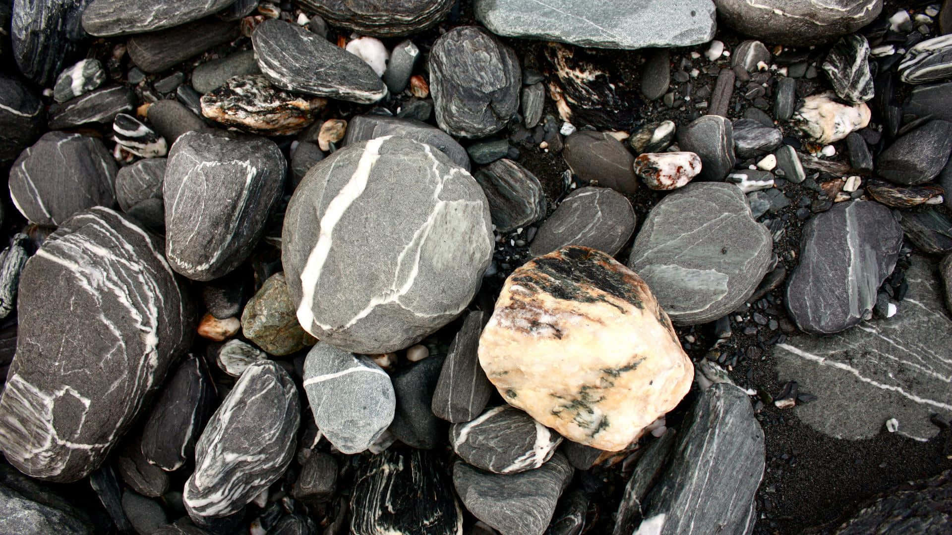 Stone 桌布 壁紙 — 光滑深灰色和白色條紋海灘石的特寫，其中有一塊奶油色米色岩石。
