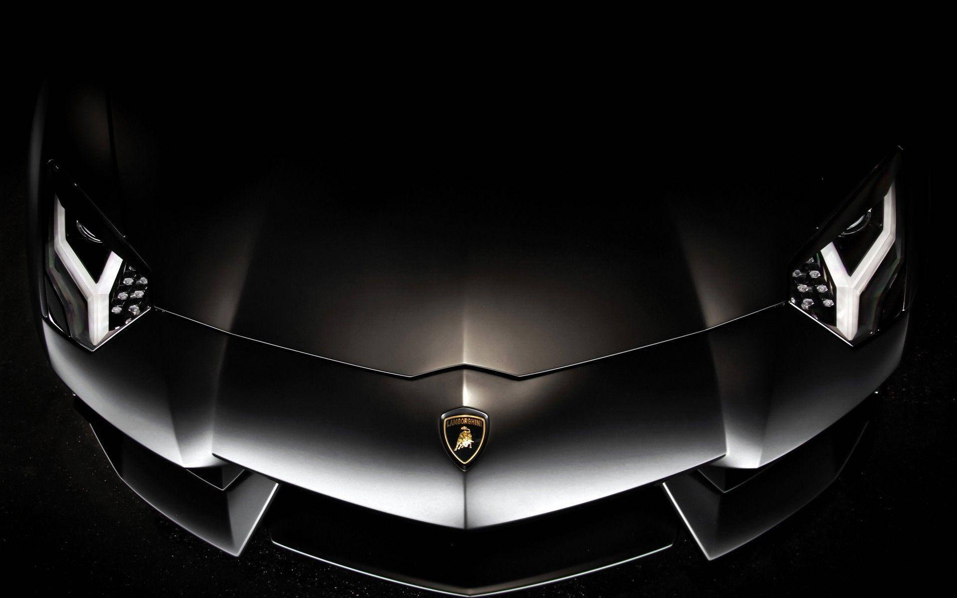 Lamborghini 4K 桌布 壁紙 — 光滑的啞光黑色藍寶堅尼前格柵，在黑暗背景下被銳利的白色頭燈照亮。