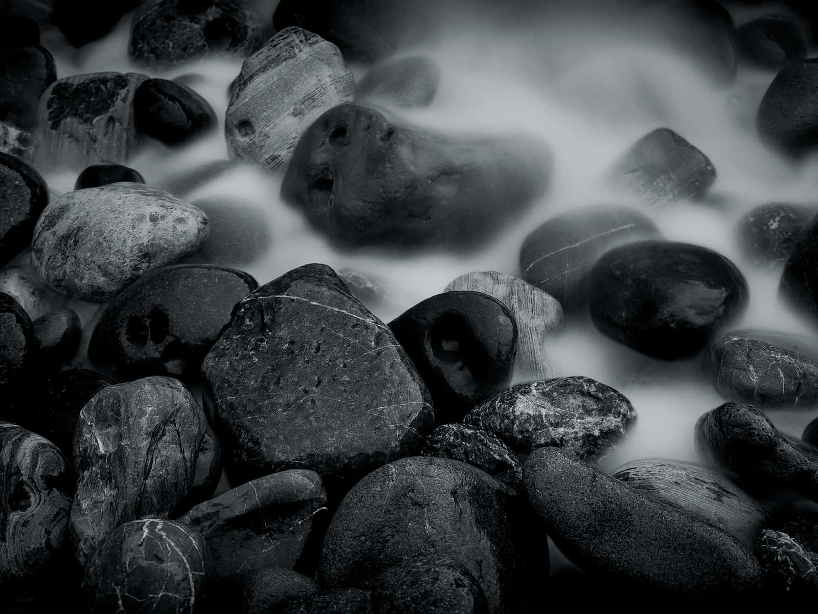 Stone 桌布 壁紙 — 光滑的深色河石從絲滑流水中浮現，呈現單色長曝光效果。