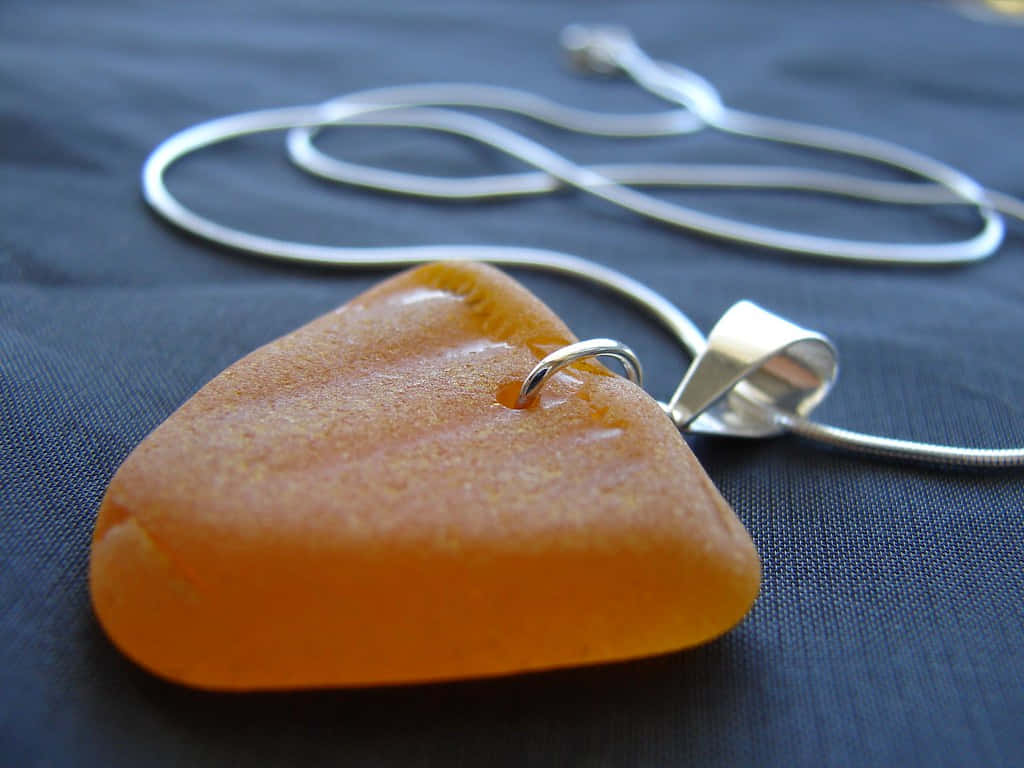 Sea Glass 桌布 壁紙 — 光滑的琥珀色海玻璃吊墜配銀鏈，放在深藍色布料上。