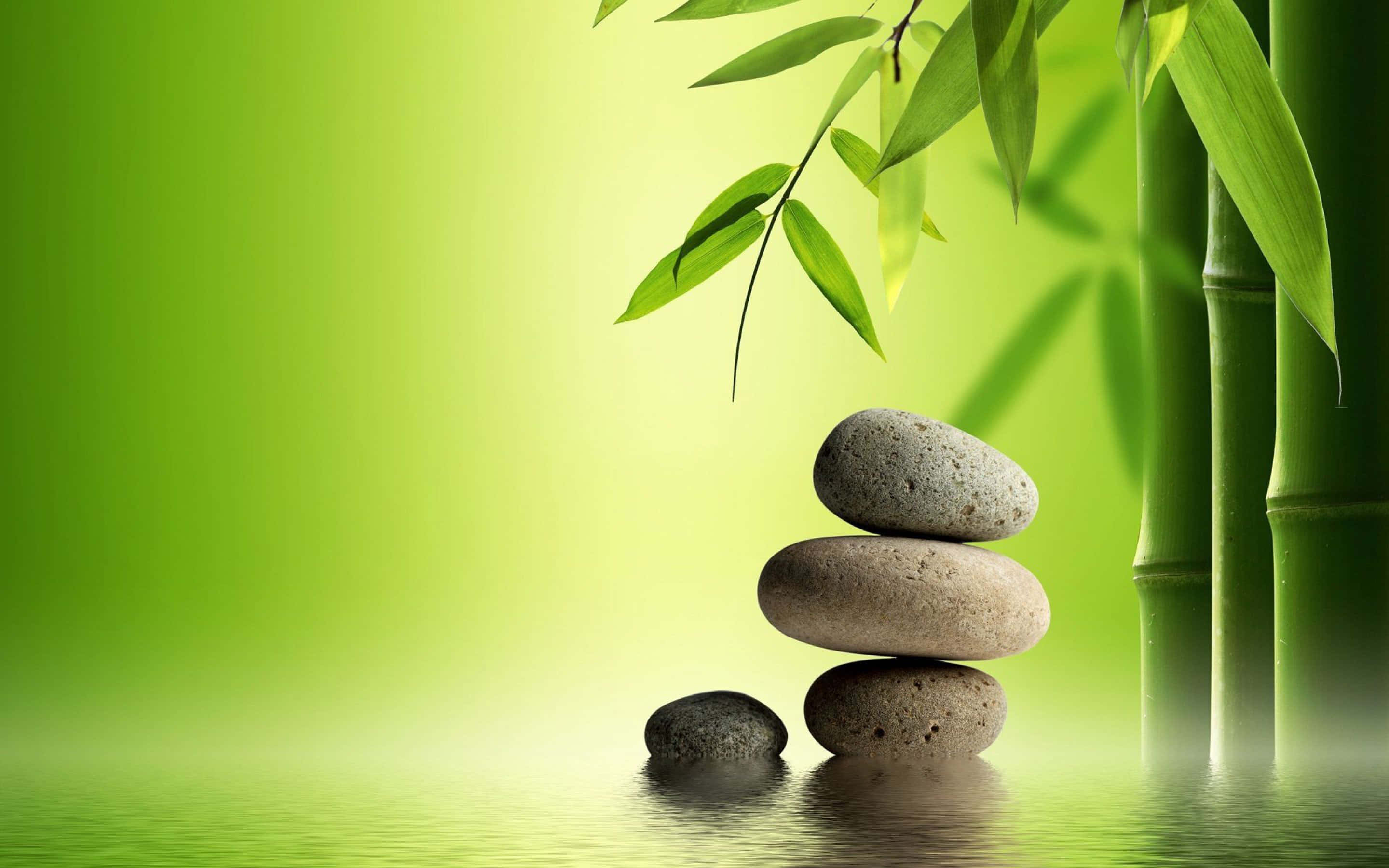禪 桌布 壁紙 — 光滑的石頭堆疊在平靜的水面上，旁邊有竹莖，在柔和的綠光下。