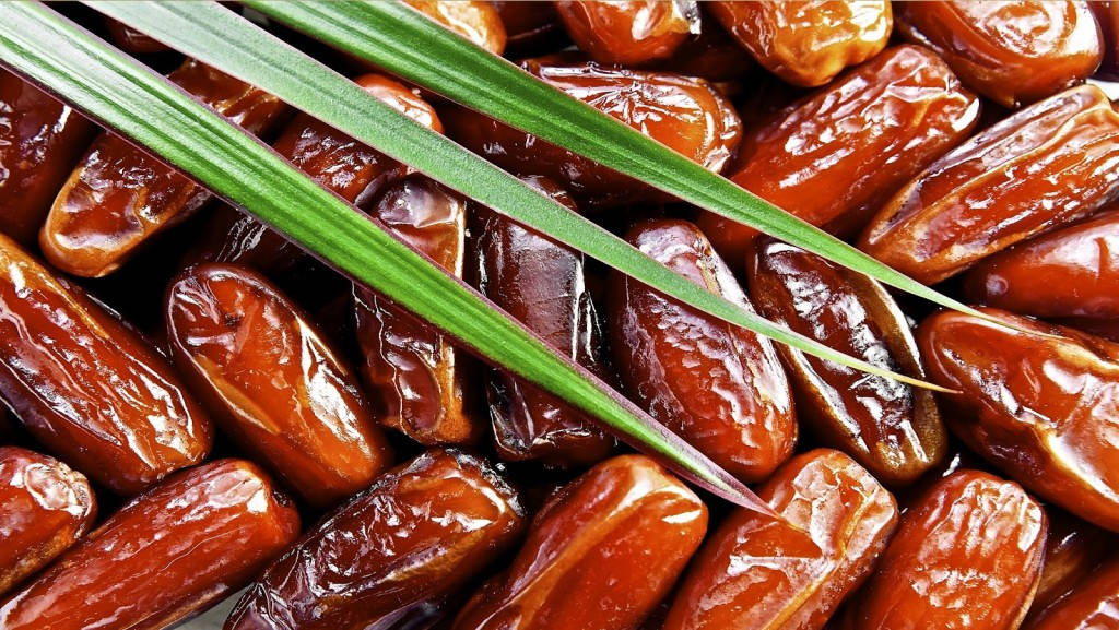 healthy 桌布 壁紙 — 光澤棕色椰棗堆疊在一起，鮮綠色棕櫚葉斜向交叉的特寫。