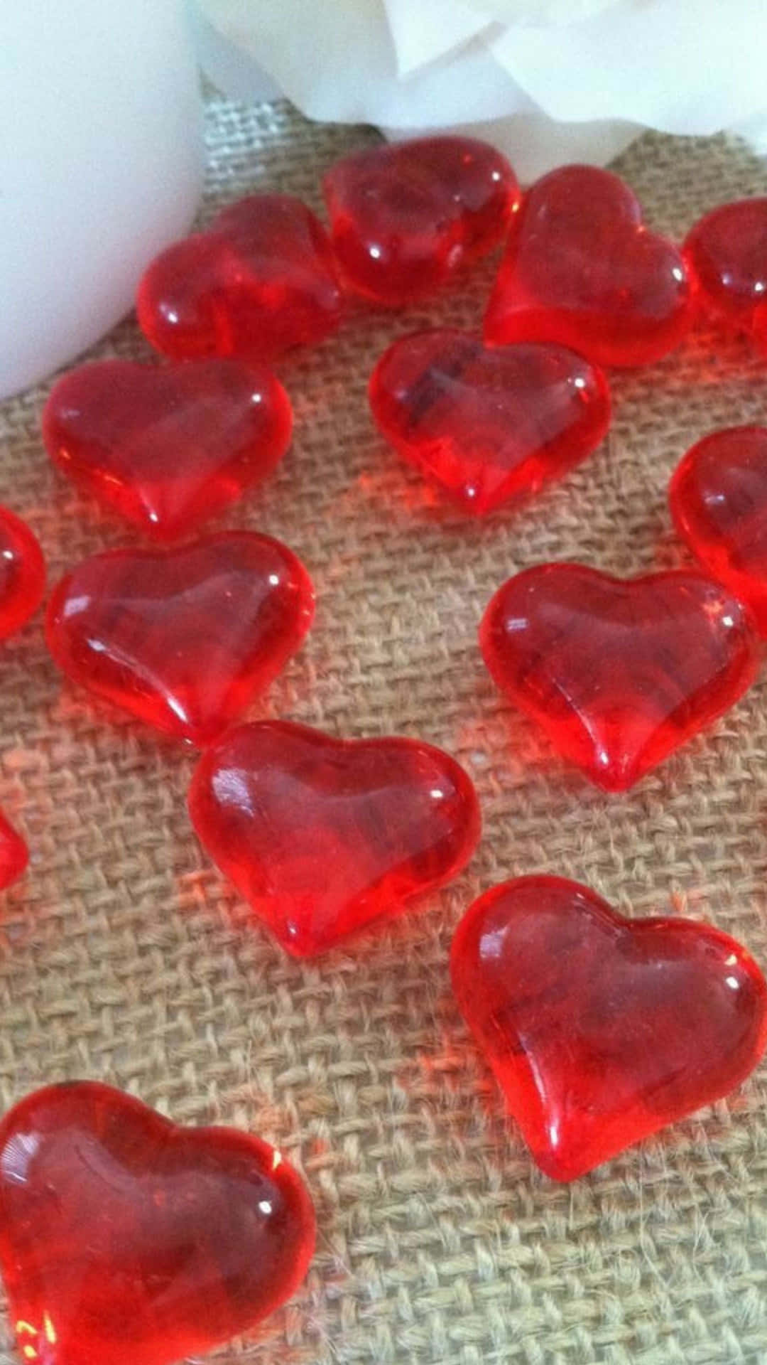 Red Hearts 桌布 壁紙 — 光澤的紅色心形糖果散落在有紋理的粗麻布上，附近有柔軟的白色花卉點綴。