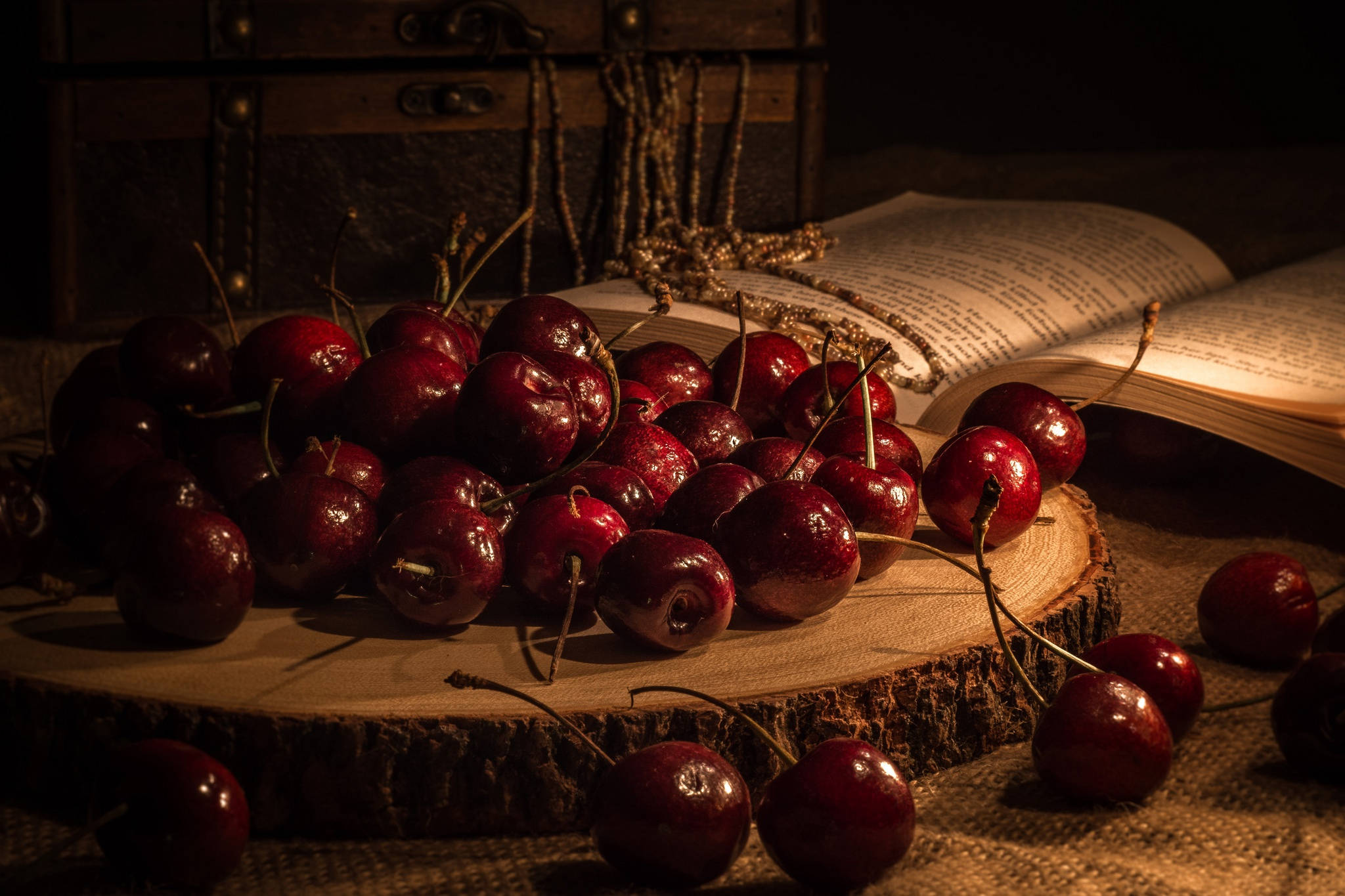 Cherry 桌布 壁紙 — 光澤的紅色櫻桃堆在木片上，旁邊有一本打開的書，在溫暖戲劇性的燈光下。