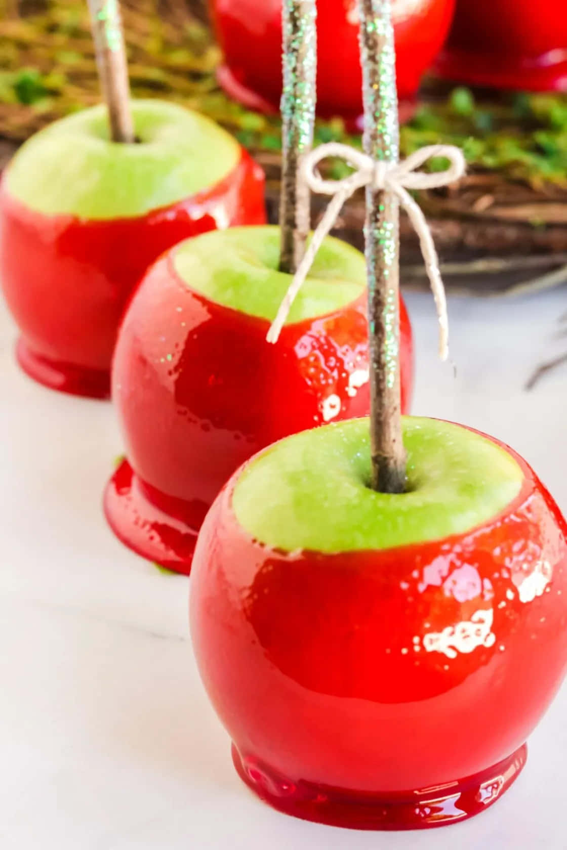 Candy Apples 桌布 壁紙 — 光澤的紅色糖果蘋果，帶有綠色莖和閃亮的棒子，放在白色表面上，用麻繩蝴蝶結繫著。