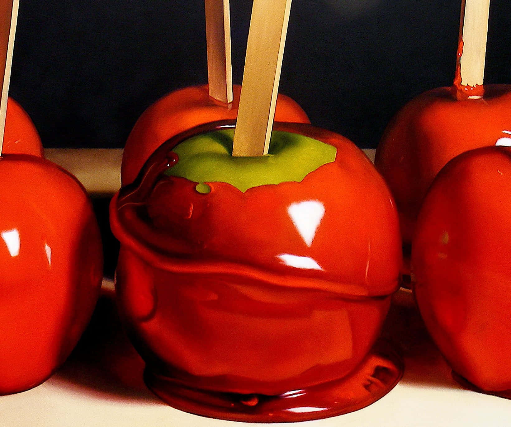 Candy Apples 桌布 壁紙 — 光澤的紅色糖果蘋果，帶有綠色莖和木棍，在深色背景上一字排開。