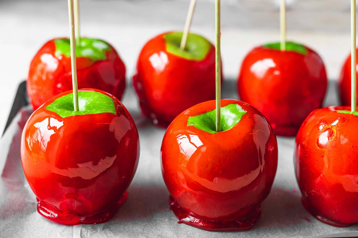 Candy Apples 桌布 壁紙 — 光澤的紅色糖果蘋果，帶有綠色莖的棒子，放在烘焙紙上，特寫鏡頭。