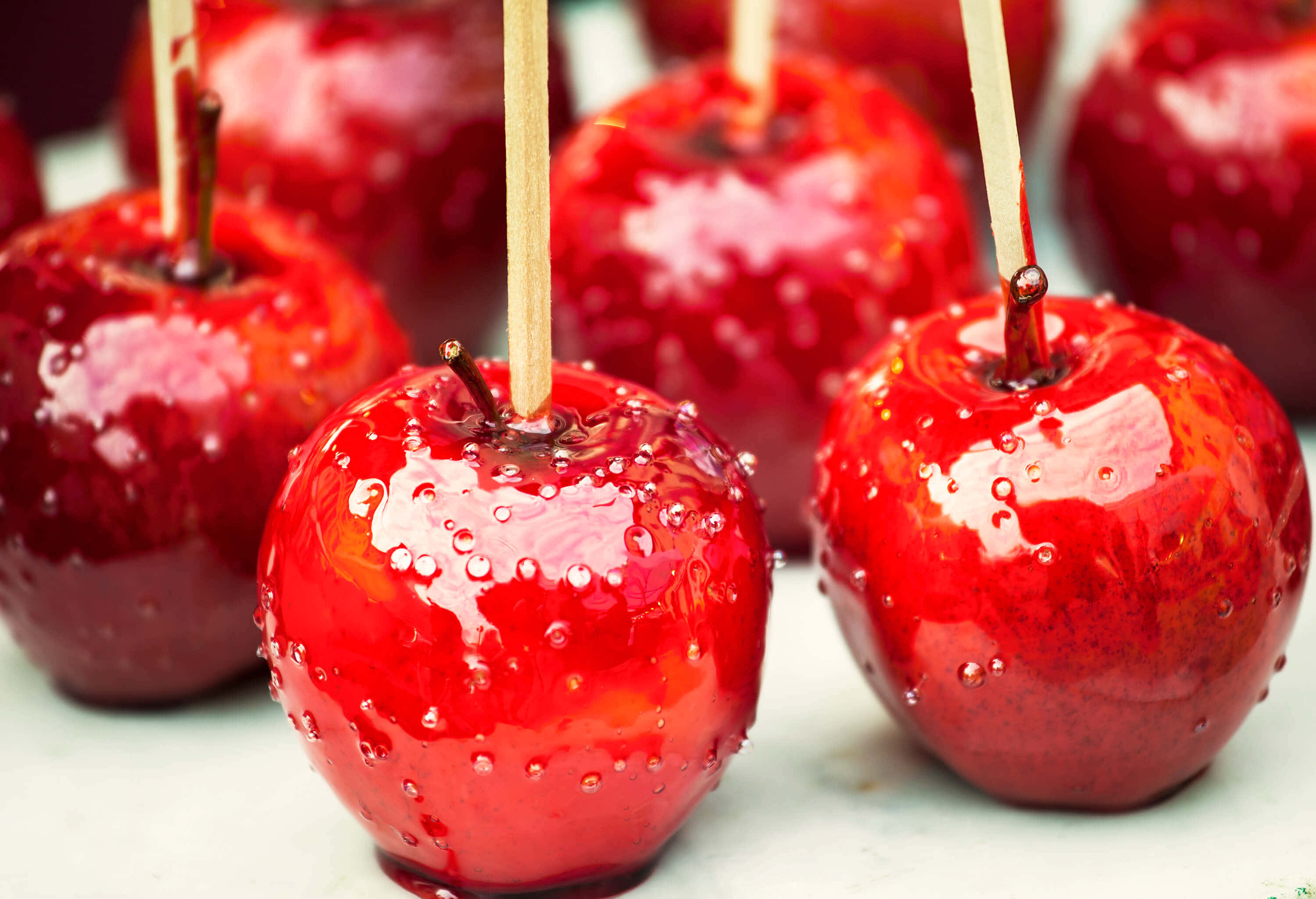 Candy Apples 桌布 壁紙 — 光澤的紅色糖蘋果配上木棍，在柔和的白色背景上閃爍著糖滴。