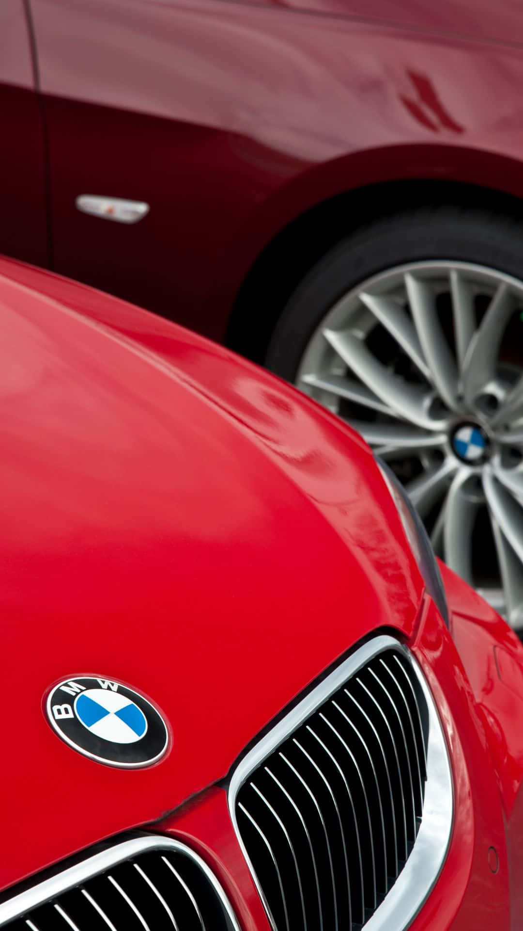Android Bmw 桌布 壁紙 — 光澤紅色BMW車頭蓋和進氣格柵的特寫，背景有一輛栗色BMW。