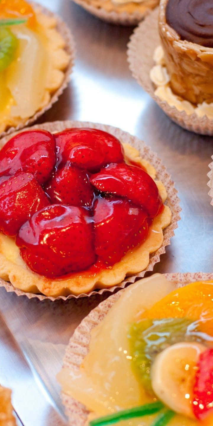 Pastry 桌布 壁紙 — 光澤草莓撻和熱帶水果撻排列在反光金屬表面上。