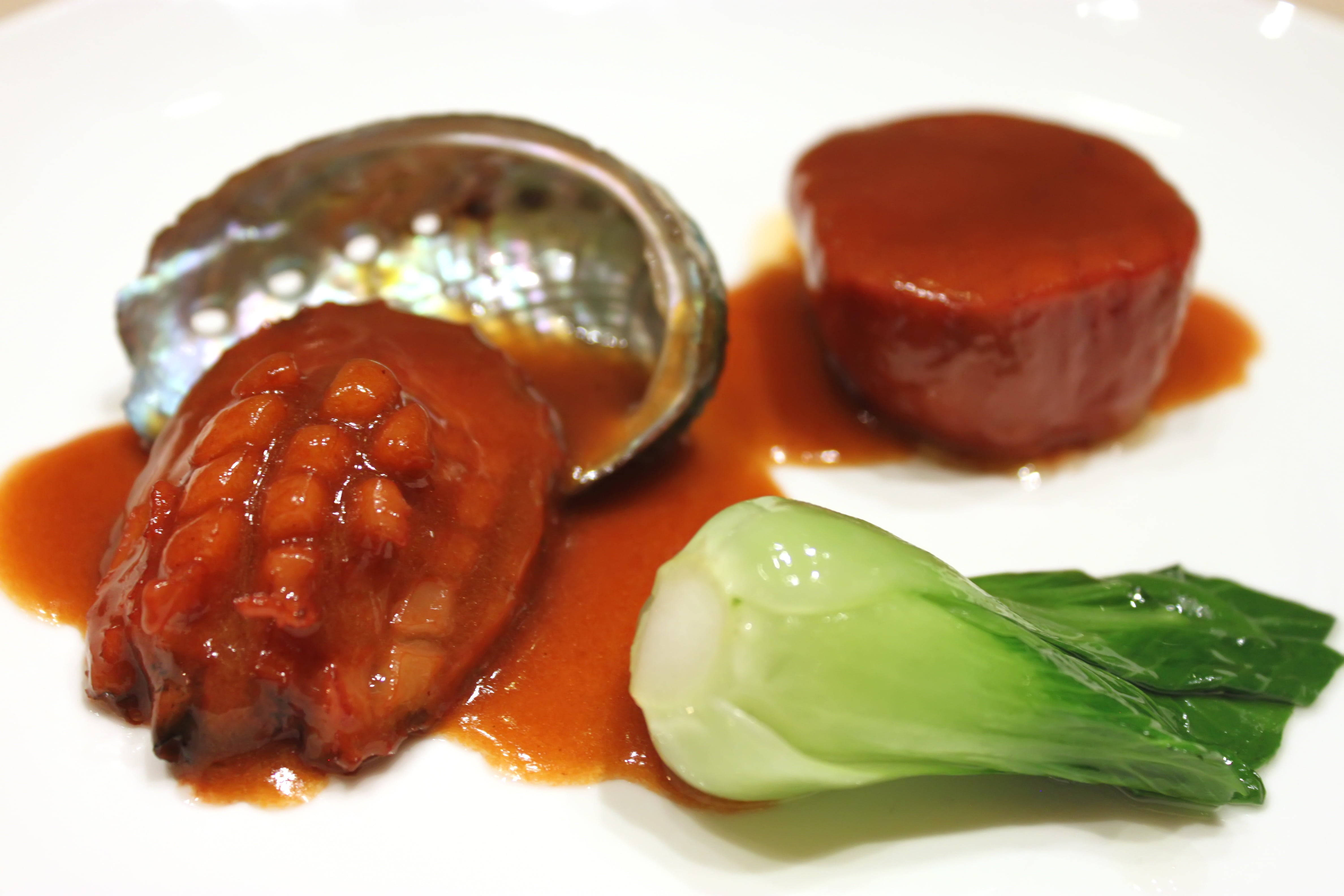 Food Photography 桌布 壁紙 — 光澤鮑魚配上濃郁醬汁，旁邊有白菜和圓形陶罐，盛載在潔白無瑕的碟子上。