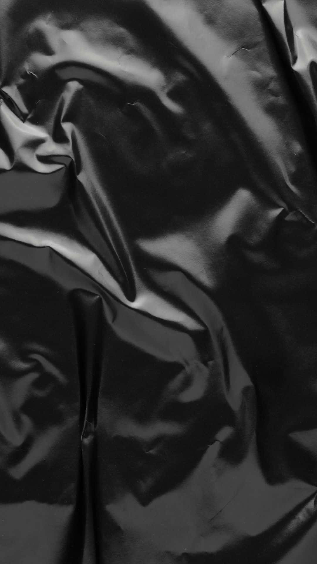 Glossy Black 桌布 壁紙 — 光澤黑色布料特寫，戲劇性的褶皺捕捉柔和光線，形成深邃陰影和明亮高光。