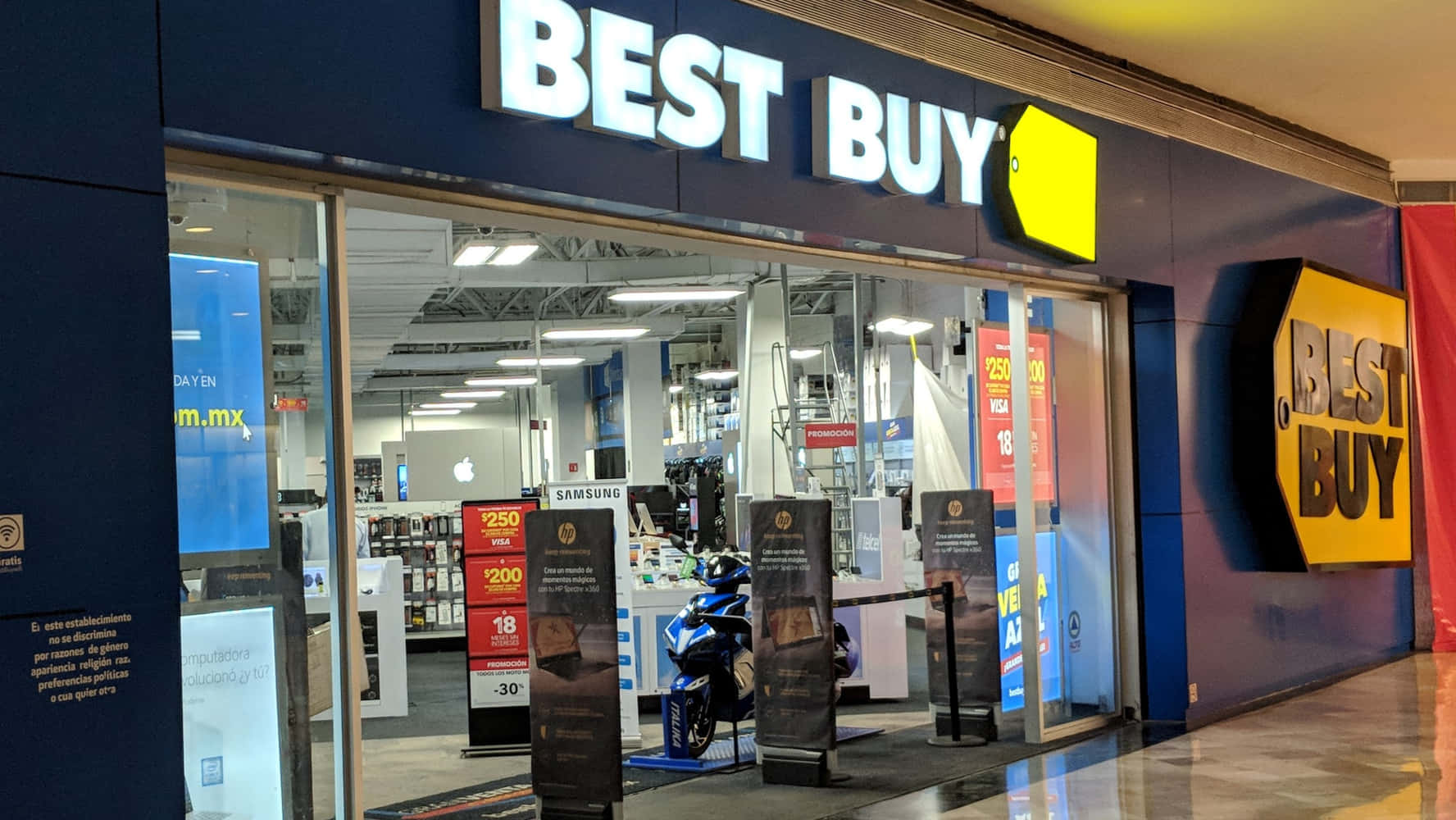 Best Buy 桌布 壁紙 — 光線充足的Best Buy商店入口，玻璃門展示內部的電子產品和促銷標誌。