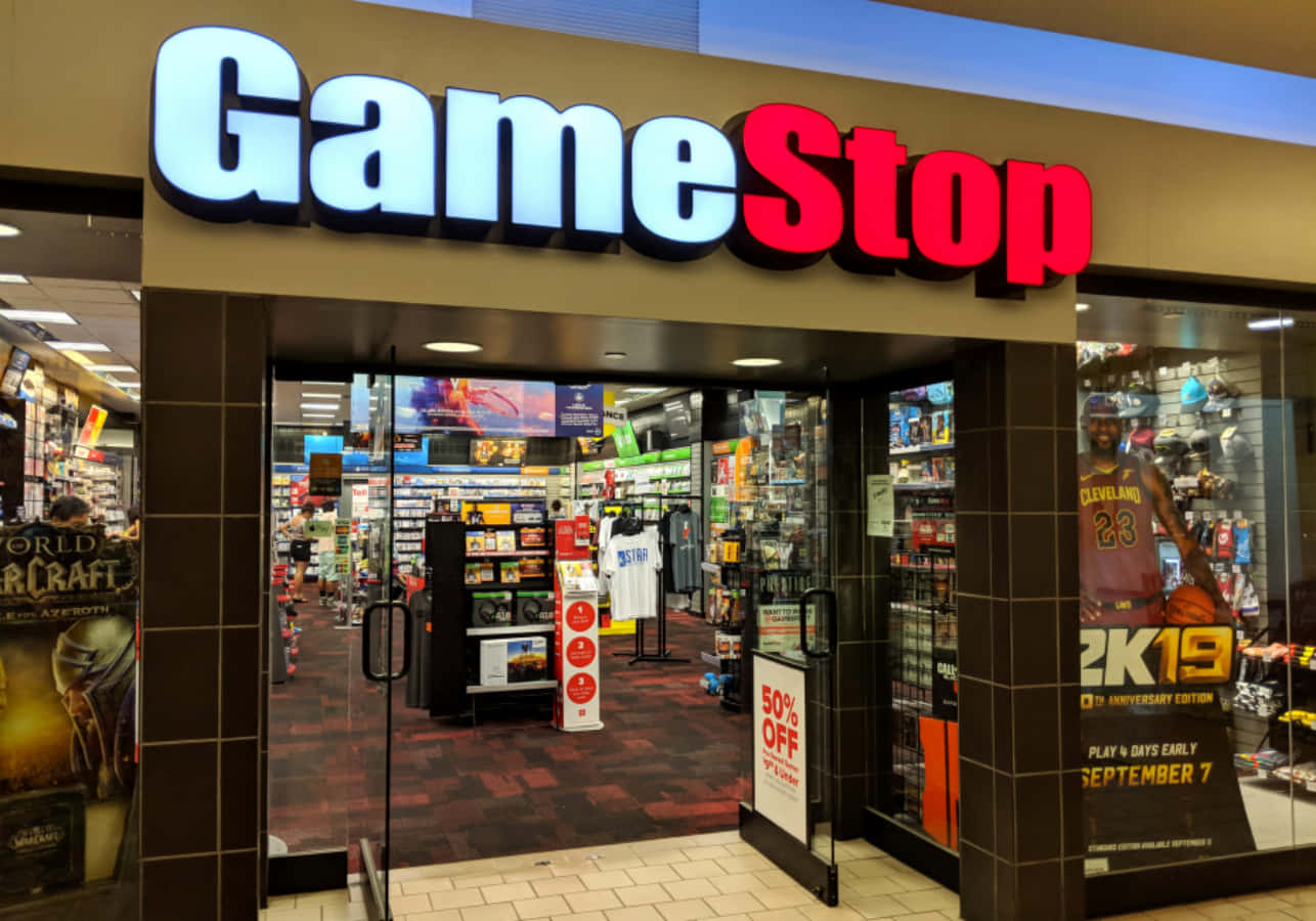 GameStop 桌布 壁紙 — 光線充足的GameStop店面，發光招牌和玻璃門展示內部的電子遊戲和商品貨架。
