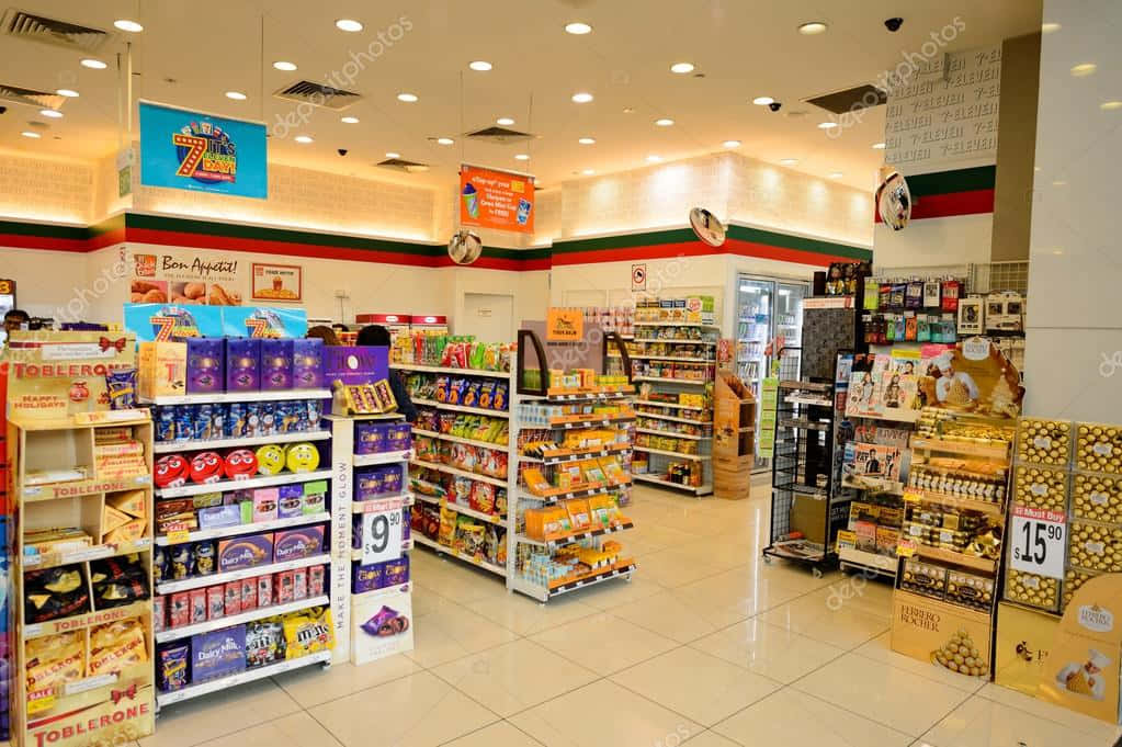 7-ELEVEN 桌布 壁紙 — 光線充足的便利商店內部，設有色彩繽紛的糖果通道和促銷標誌，上方是明亮的天花板燈。