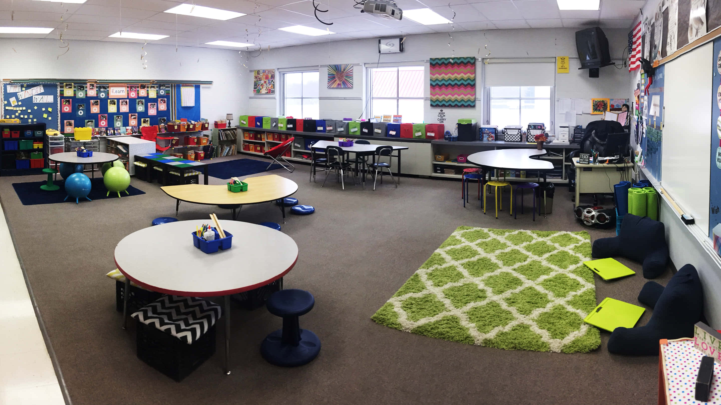 Classroom 桌布 壁紙 — 光線充足的小學教室，配有色彩繽紛的圓桌、椅子、地毯和牆上的教育裝飾。