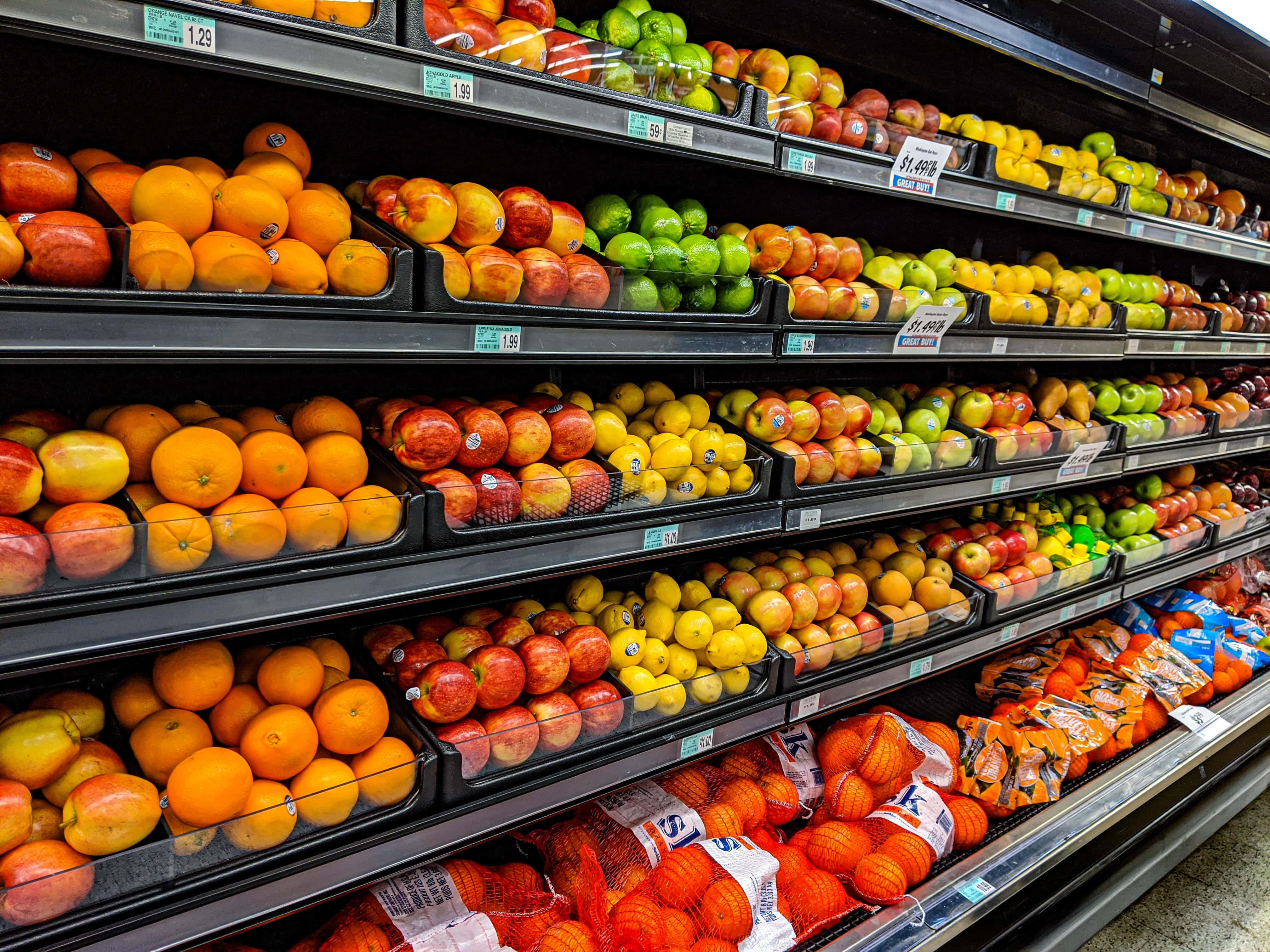 Fruits 桌布 壁紙 — 光線充足的雜貨店貨架上擺滿了鮮豔的柳橙、蘋果和檸檬。