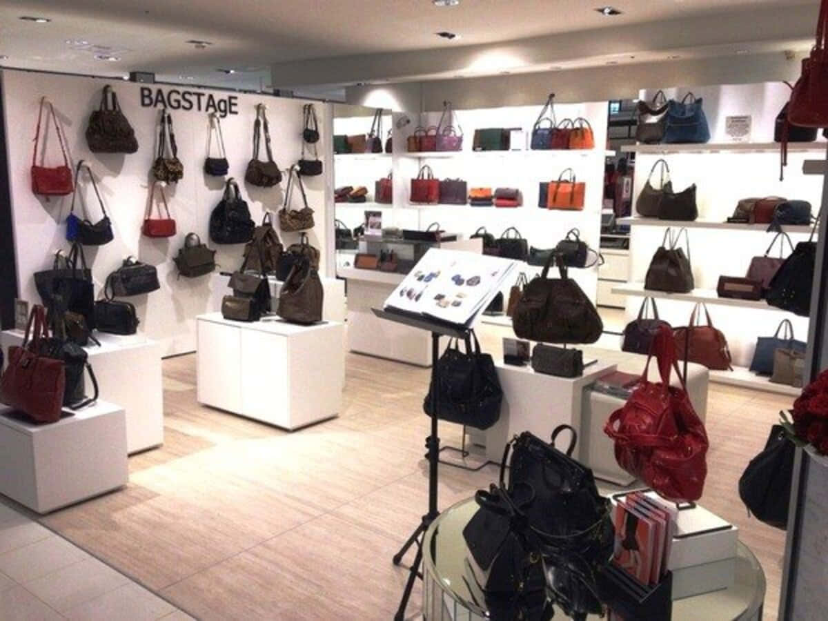Store 桌布 壁紙 — 光線充足的零售店在白色貨架和底座上展示色彩繽紛的手提包，上方有明亮的吊燈。