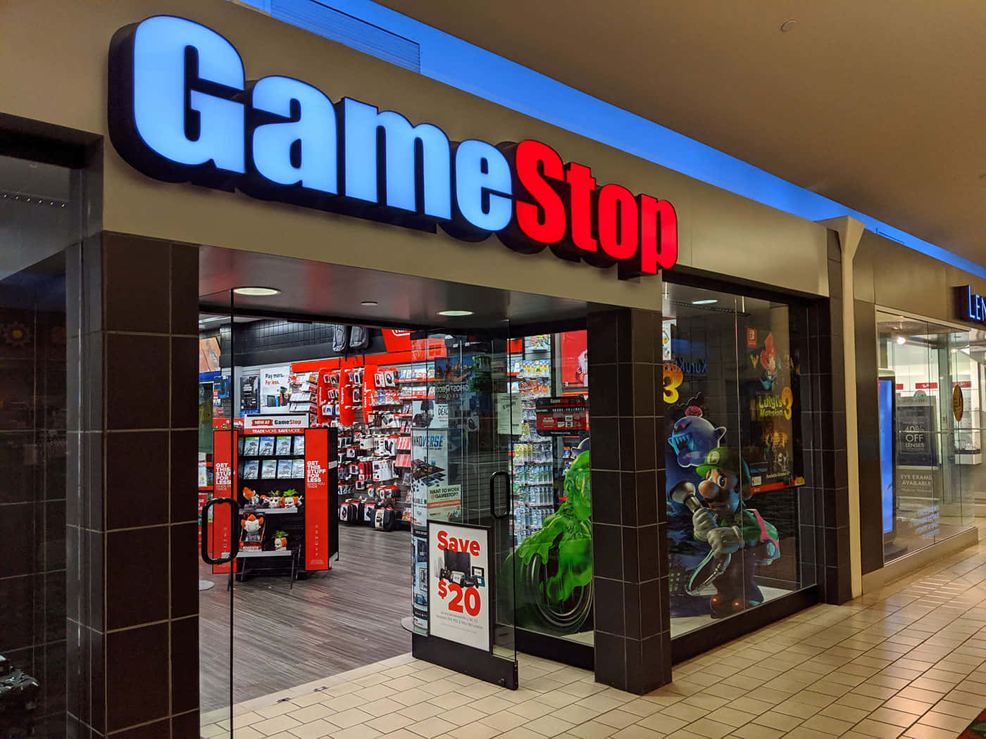 GameStop 桌布 壁紙 — 光線明亮的GameStop店鋪正面，玻璃門窗展示商場內色彩繽紛的電玩商品和角色立牌。