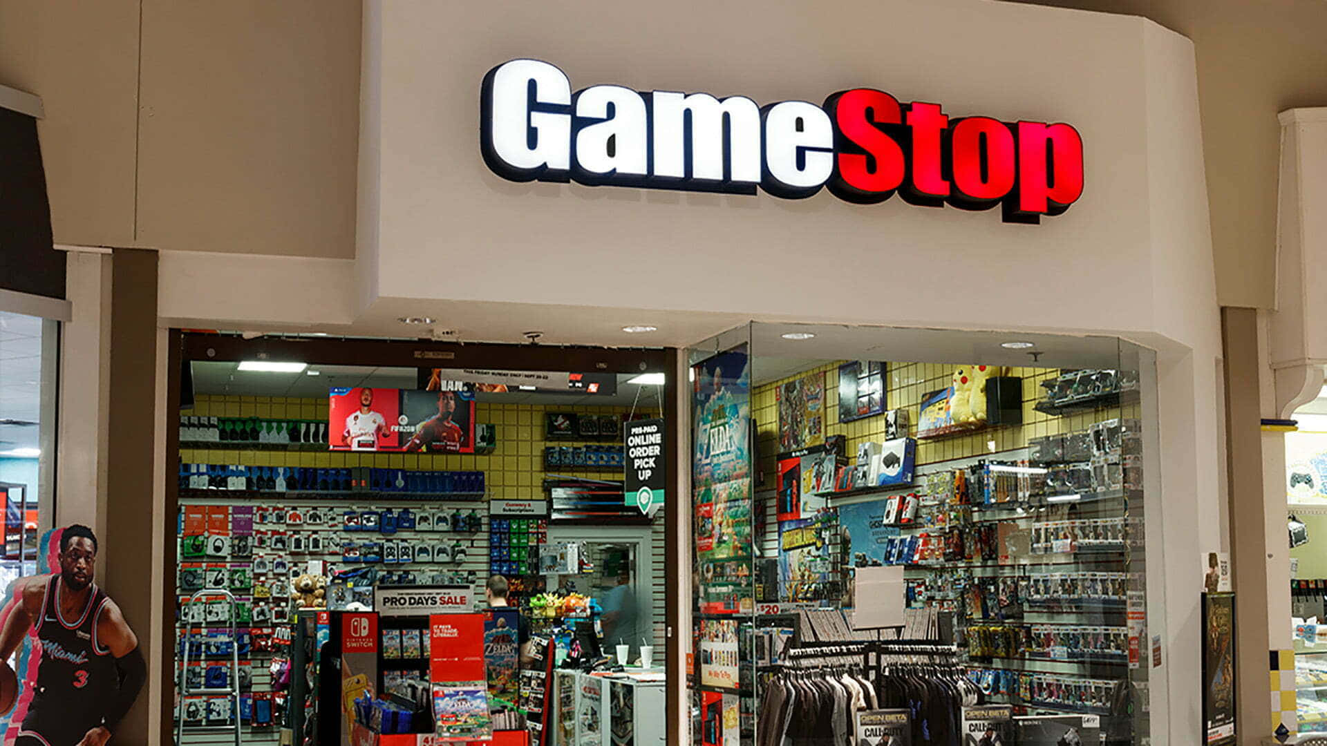 GameStop 桌布 壁紙 — 光線明亮的GameStop店面，玻璃門內可見貨架上擺滿了電玩遊戲和商品。