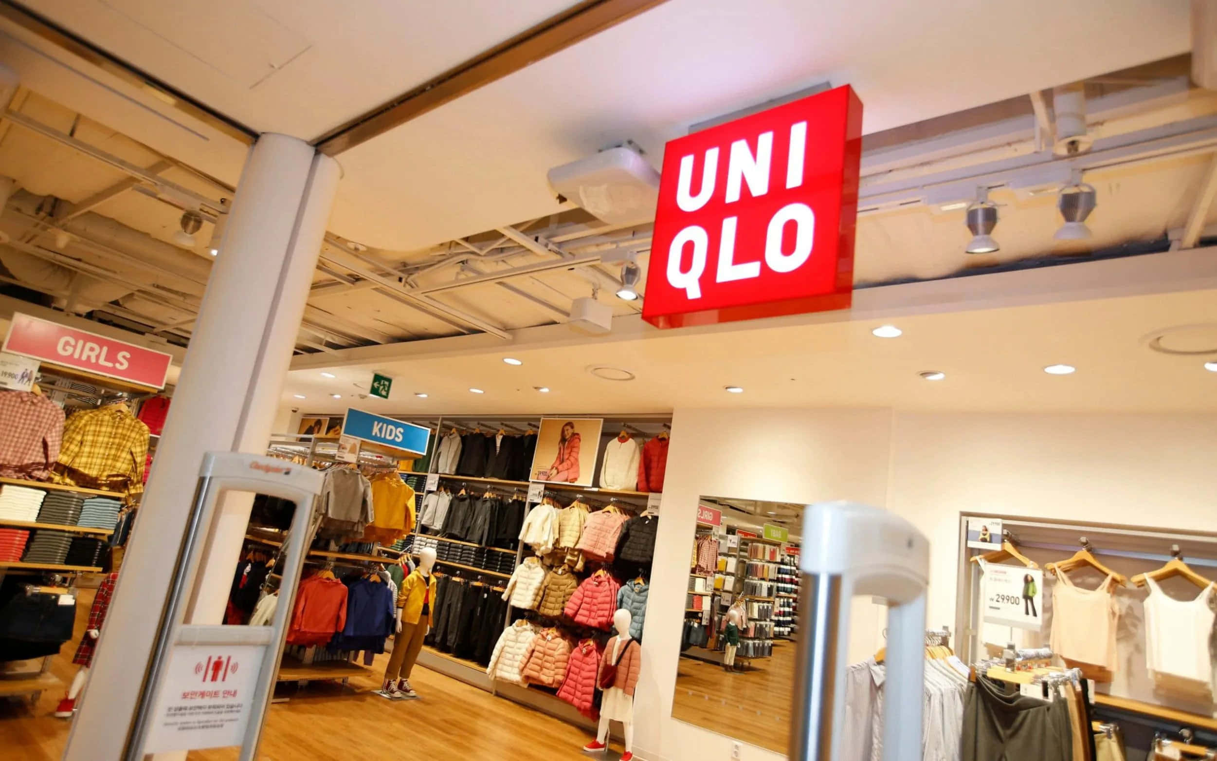 Uniqlo 桌布 壁紙 — 光線明亮的UNIQLO店鋪內部，設有服裝陳列架和一個從天花板懸掛的顯眼紅色招牌。