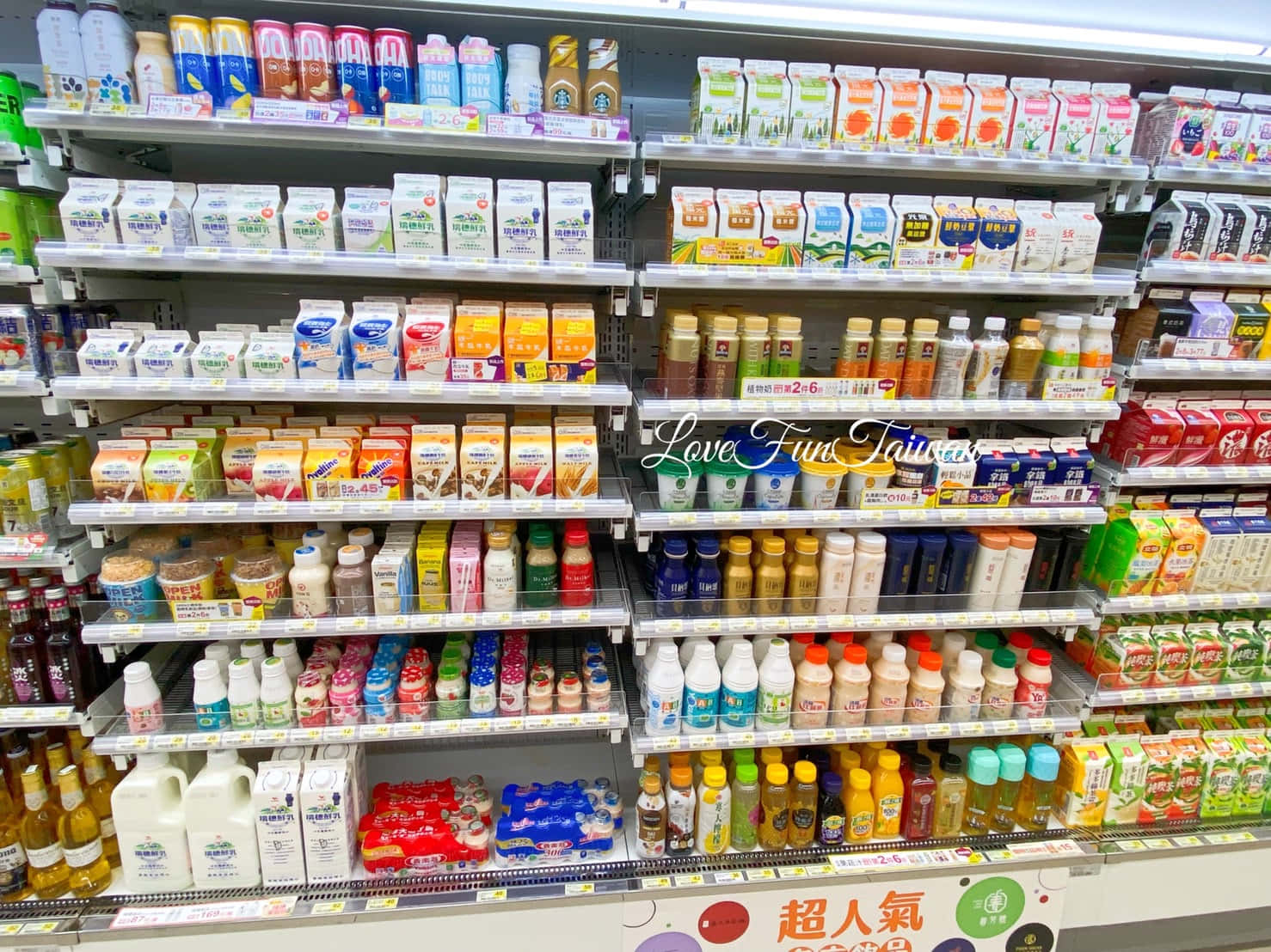 7-ELEVEN 桌布 壁紙 — 光線明亮的超市通道，金屬貨架上擺滿了色彩繽紛的瓶裝和盒裝飲料。