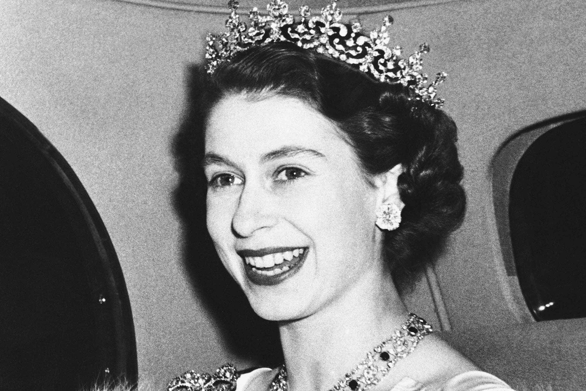 Queen 桌布 壁紙 — 光芒四射的伊麗莎白二世女王在飛機艙內佩戴閃爍的頭飾和鑽石珠寶，溫暖地微笑。