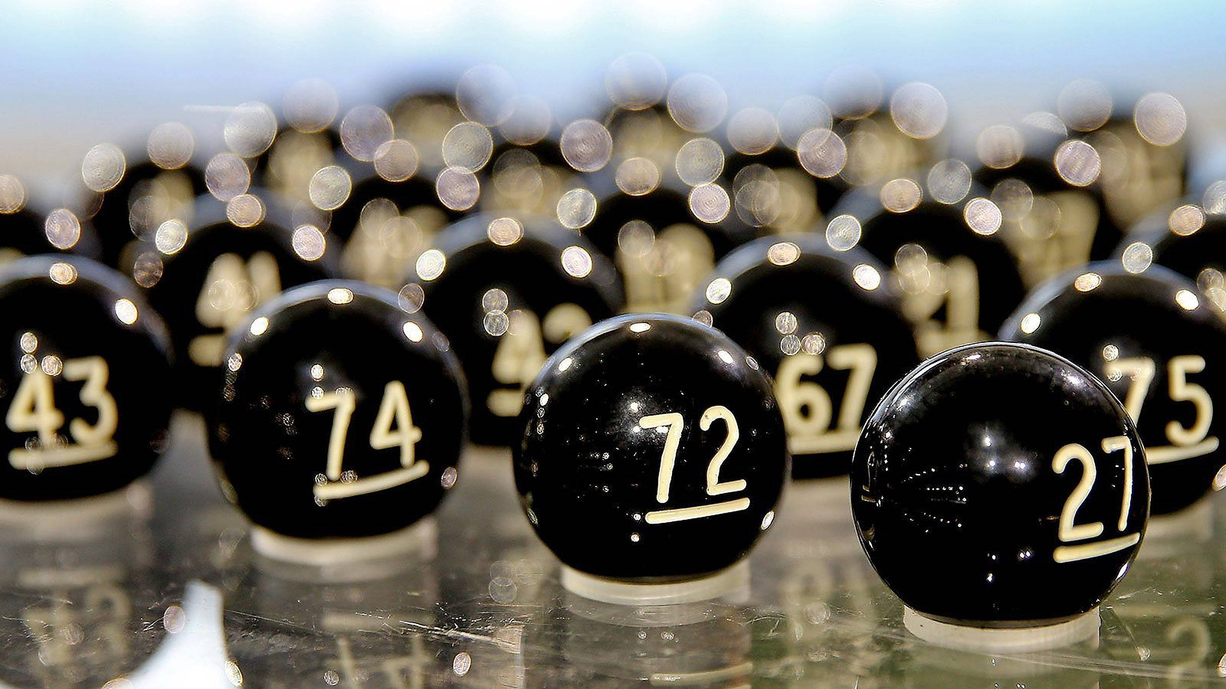 Lottery 桌布 壁紙 — 光面黑色彩票球帶白色數字，特寫，放置在反光表面上，背景燈光模糊。