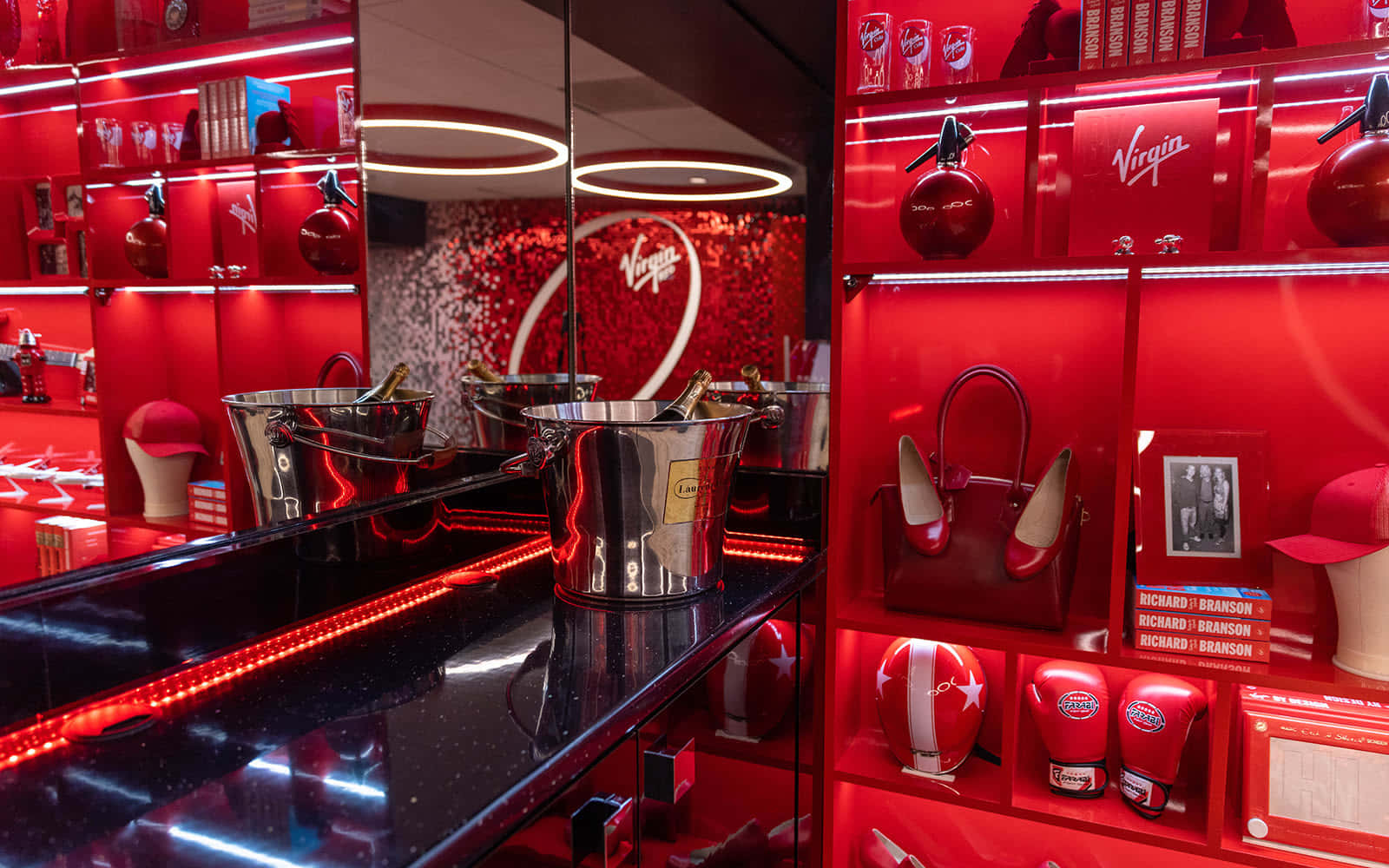 Red Room 桌布 壁紙 — 光面黑色櫃檯反射出充滿維珍品牌商品和香檳桶的鮮紅色貨架，在霓虹燈光下。