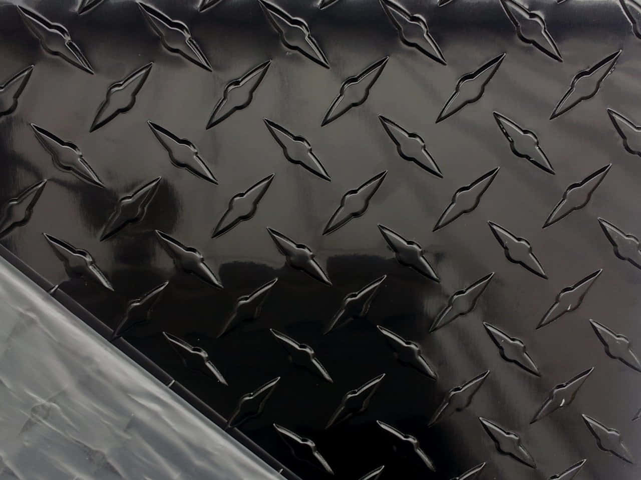 Diamond Plate 桌布 壁紙 — 光面黑色菱形板金屬的特寫，帶有銳利的凸起圖案反射光線。