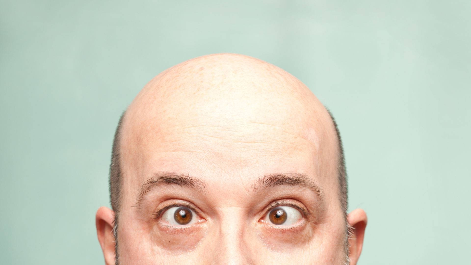Eyes 桌布 壁紙 — 光頭男士臉部特寫，一雙棕色大眼睛在淡綠色背景前傳達驚訝之情。