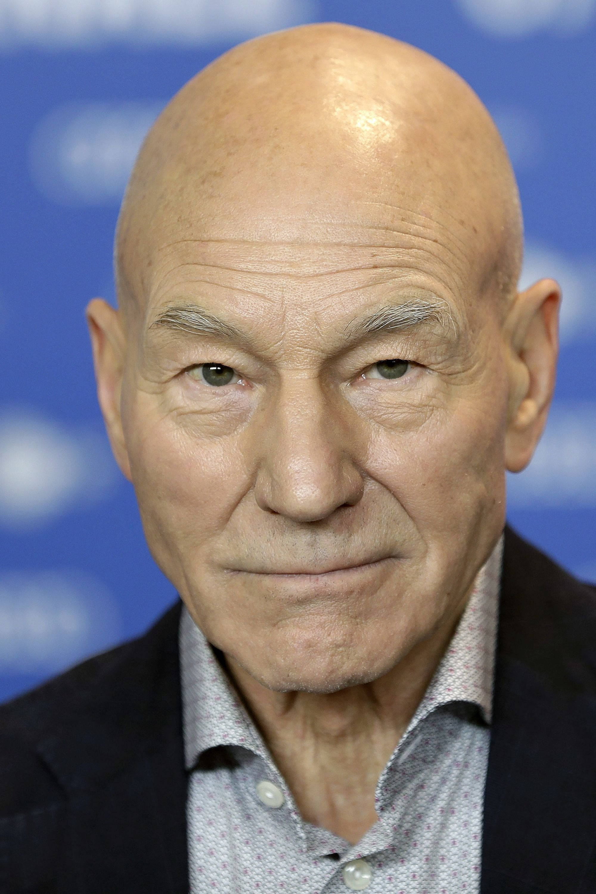 Celebrity 桌布 壁紙 — 光頭男子特寫肖像，臉上帶有深刻皺紋，表情平靜，背景為模糊的藍色。