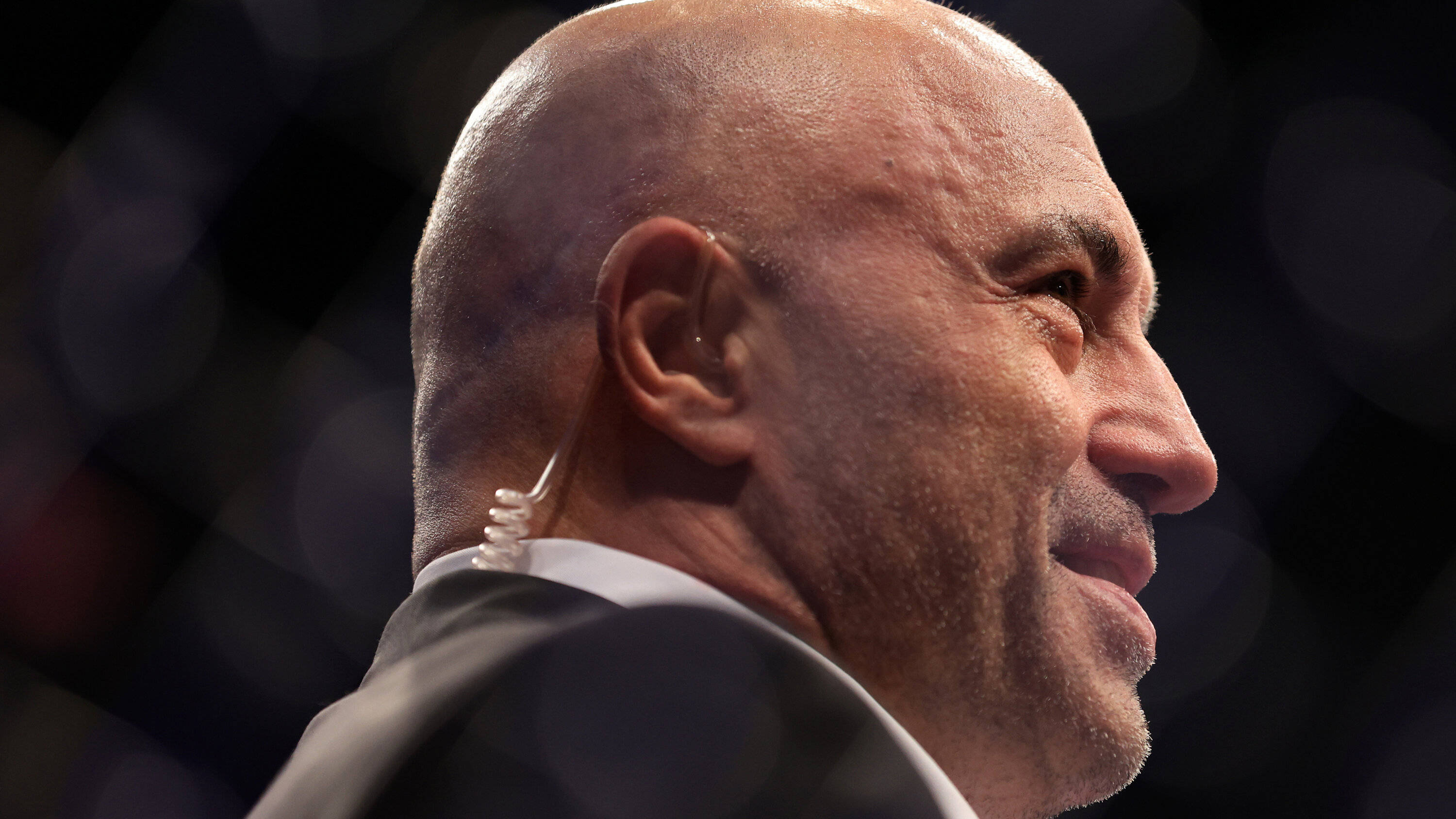 UFC 桌布 壁紙 — 光頭男子身穿西裝微笑的特寫側面，背景為模糊的八角形圍欄。