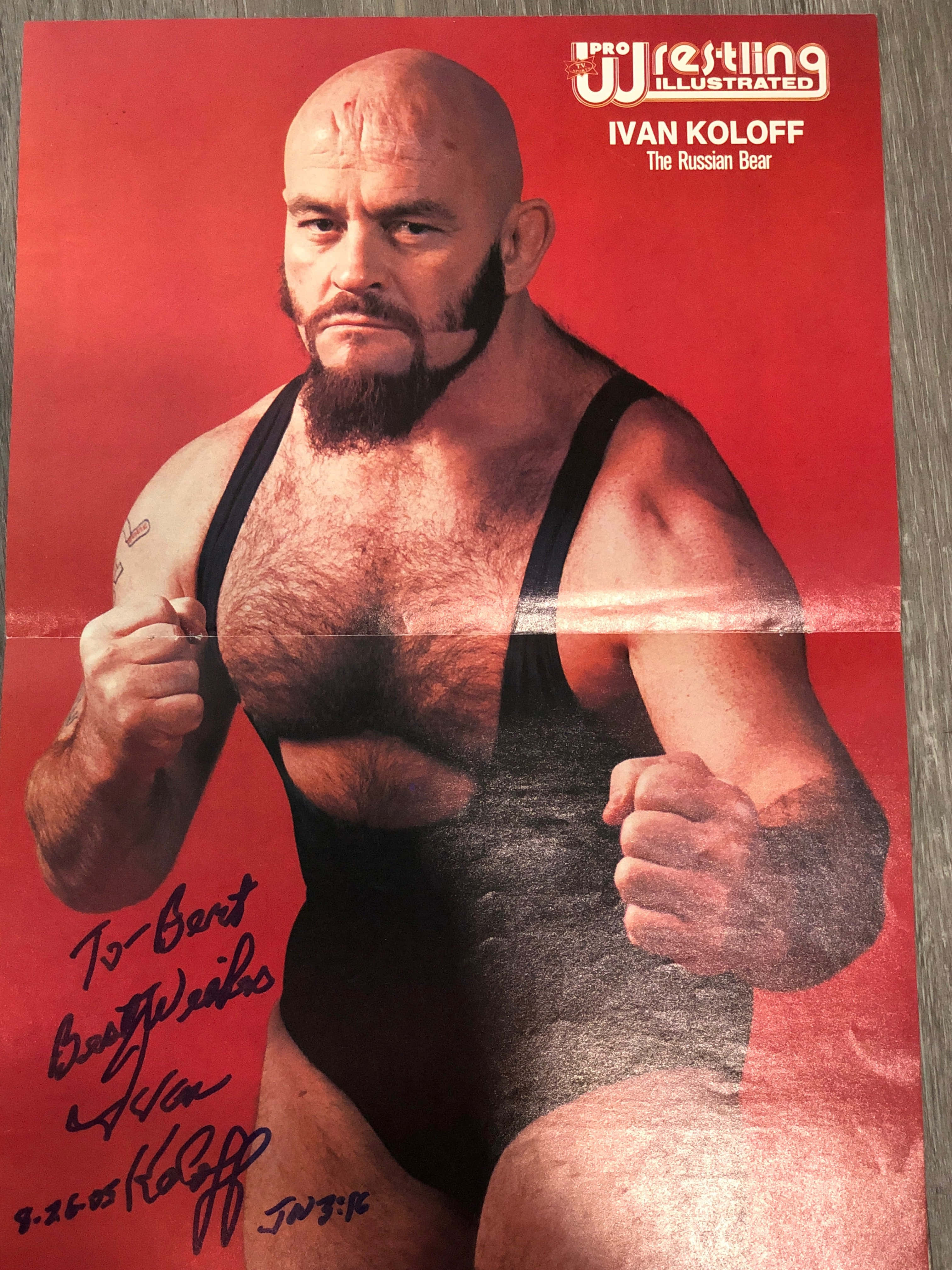 Canadian 桌布 壁紙 — 光頭鬍鬚摔角手 Ivan Koloff 身穿黑色緊身衣，在紅色背景前強烈擺姿勢，印於一張親筆簽名的 Pro Wrestling Illustrated 海報上。