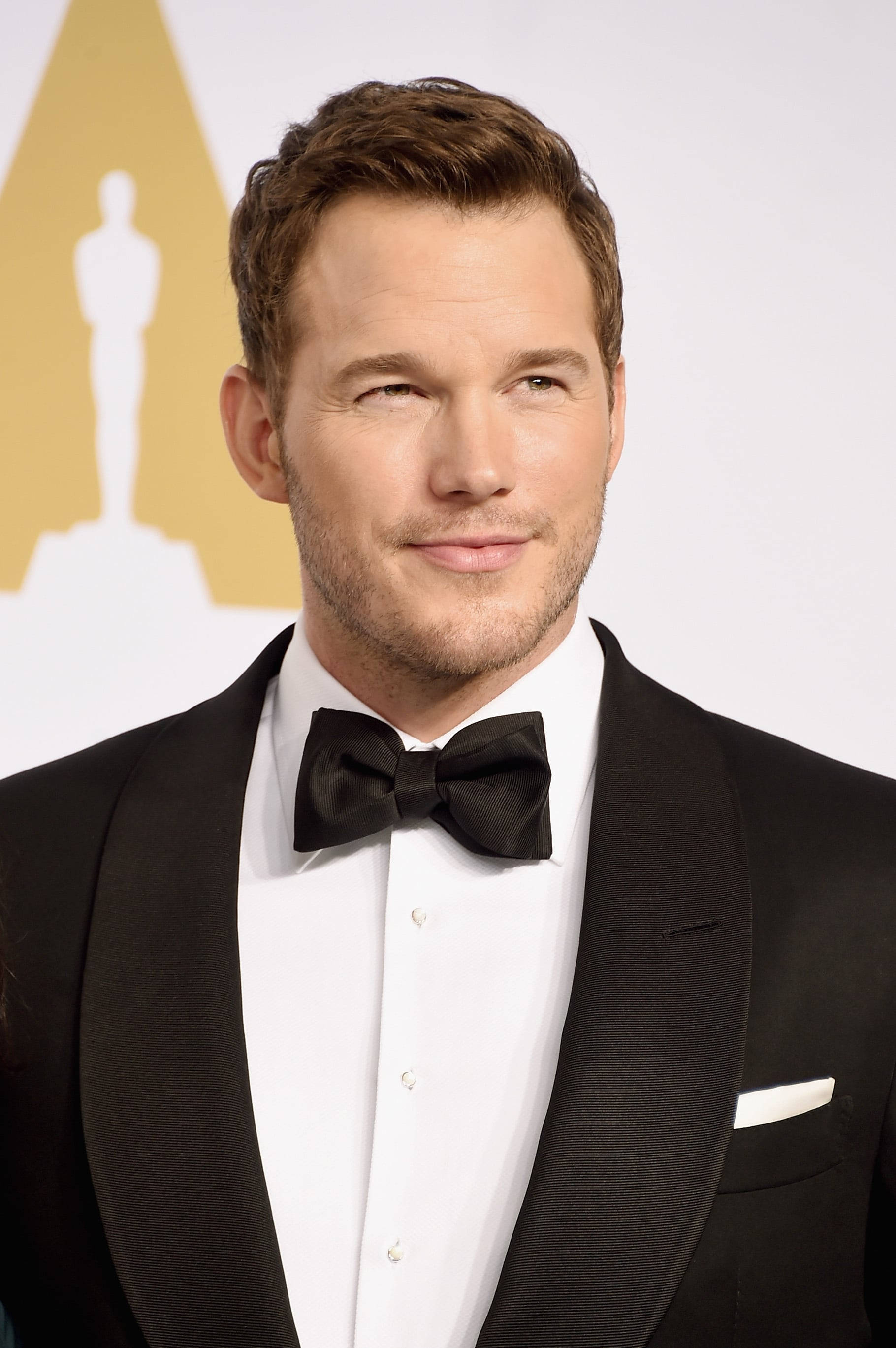 Chris Pratt 桌布 壁紙 — 克里斯普瑞特在奧斯卡背景下自信微笑，穿著黑色燕尾服和領結。