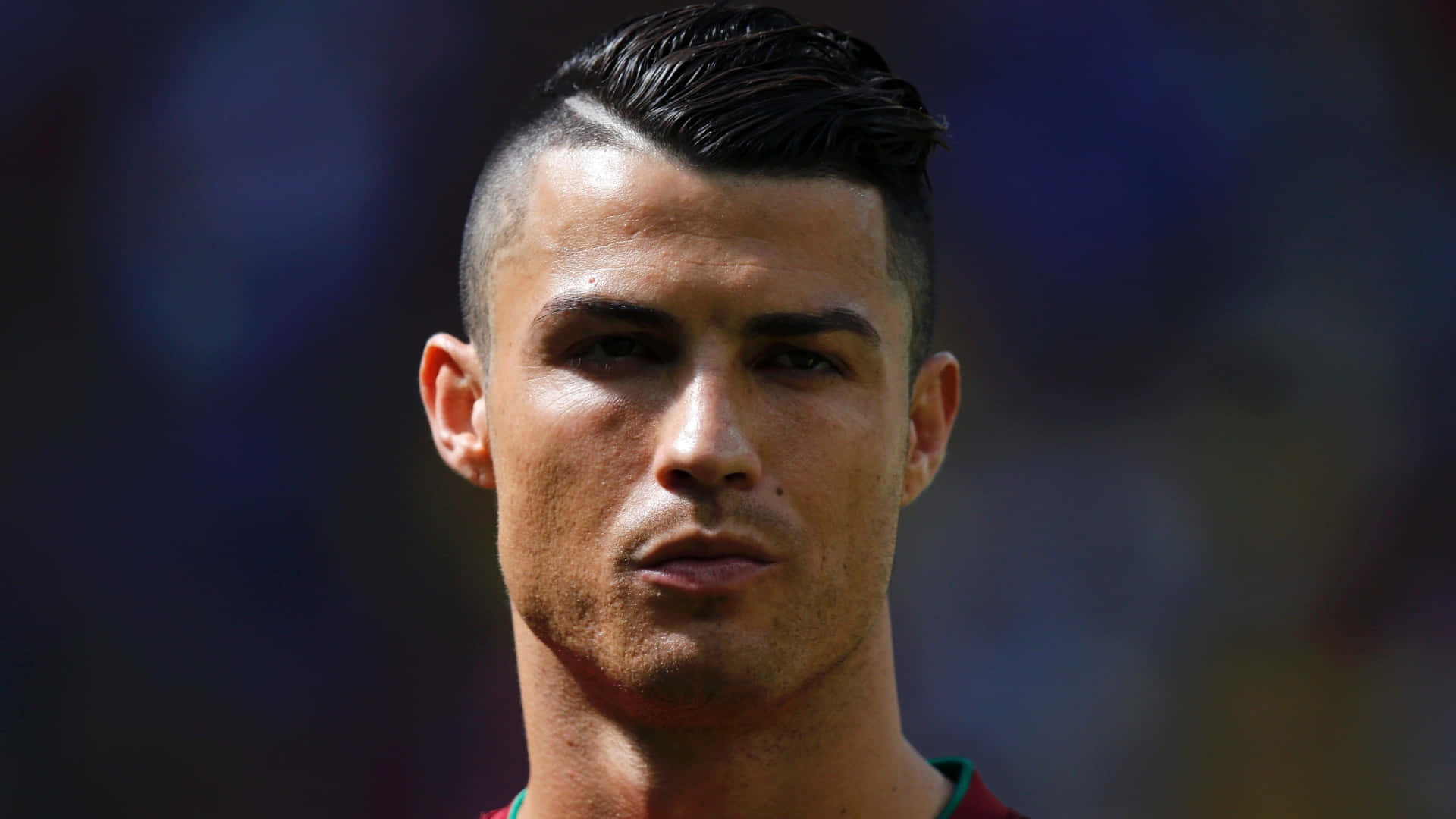 Ronaldo 桌布 壁紙 — 克里斯蒂亞諾·羅納度的特寫肖像，帶有銳利的髮型和強烈的眼神，背景是模糊的球場。