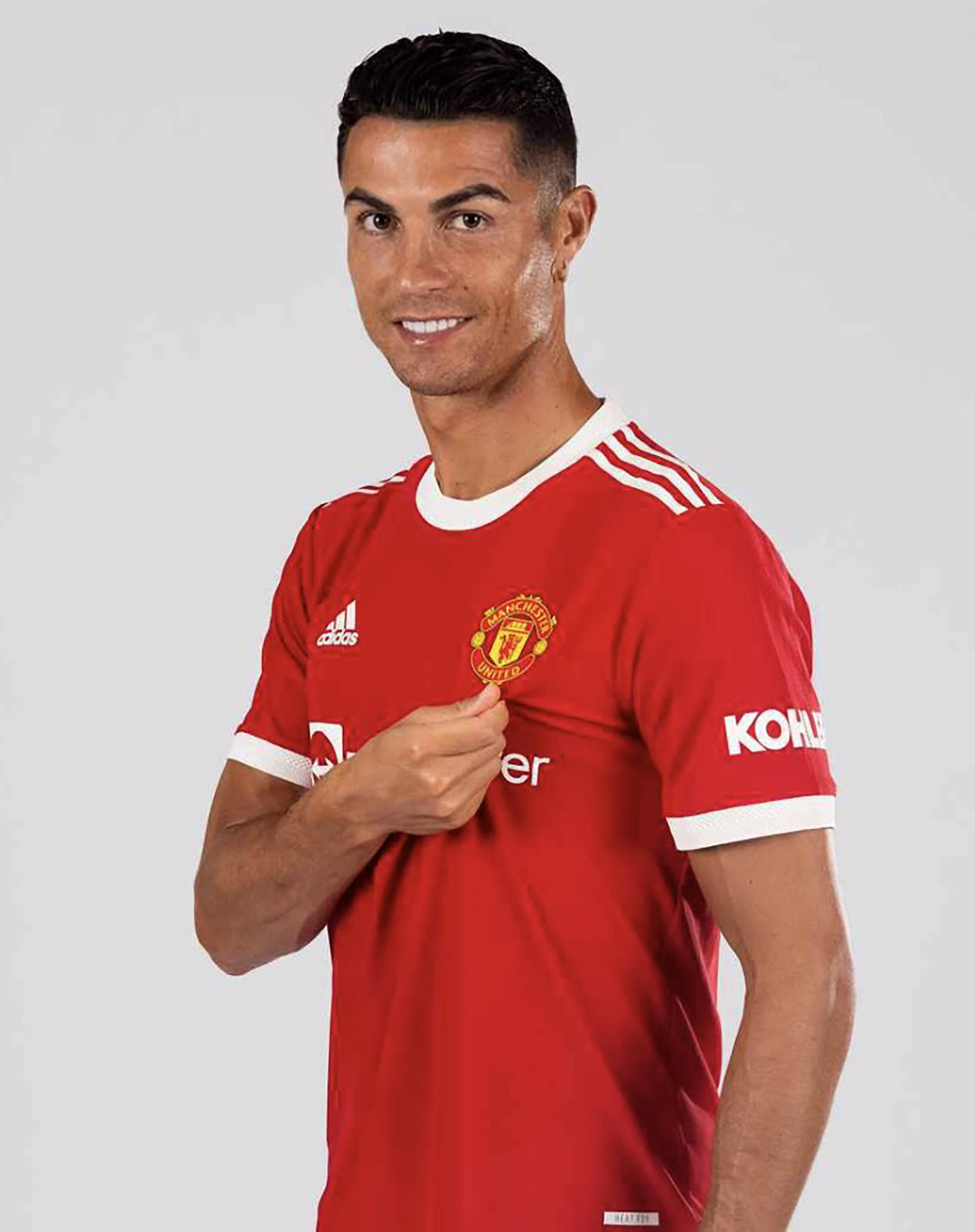 Ronaldo 桌布 壁紙 — 克里斯蒂亞諾·羅納度自信地微笑，同時觸摸他紅色球衣上的曼聯會徽，背景為純灰色。
