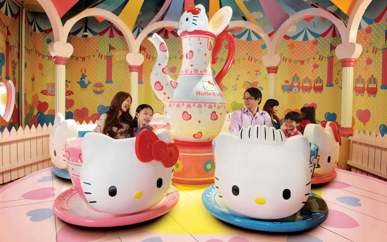 Hello Kitty 桌布 壁紙 — 兒童和成人乘坐巨大的Hello Kitty茶杯遊樂設施，在色彩繽紛、夢幻的主題公園景點中。